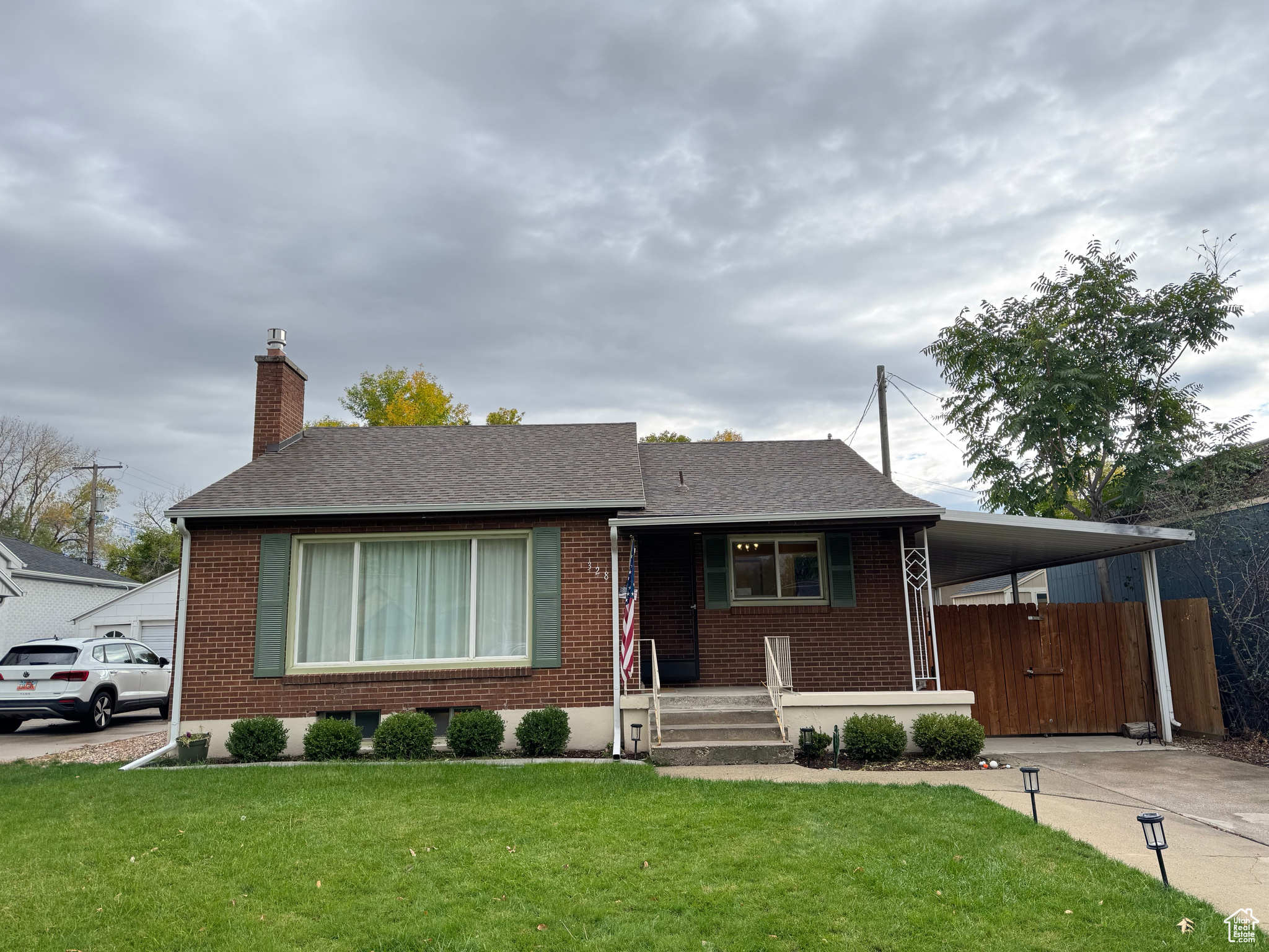 View of front of house featuring an attached carport, brick siding, driveway, and a front yard