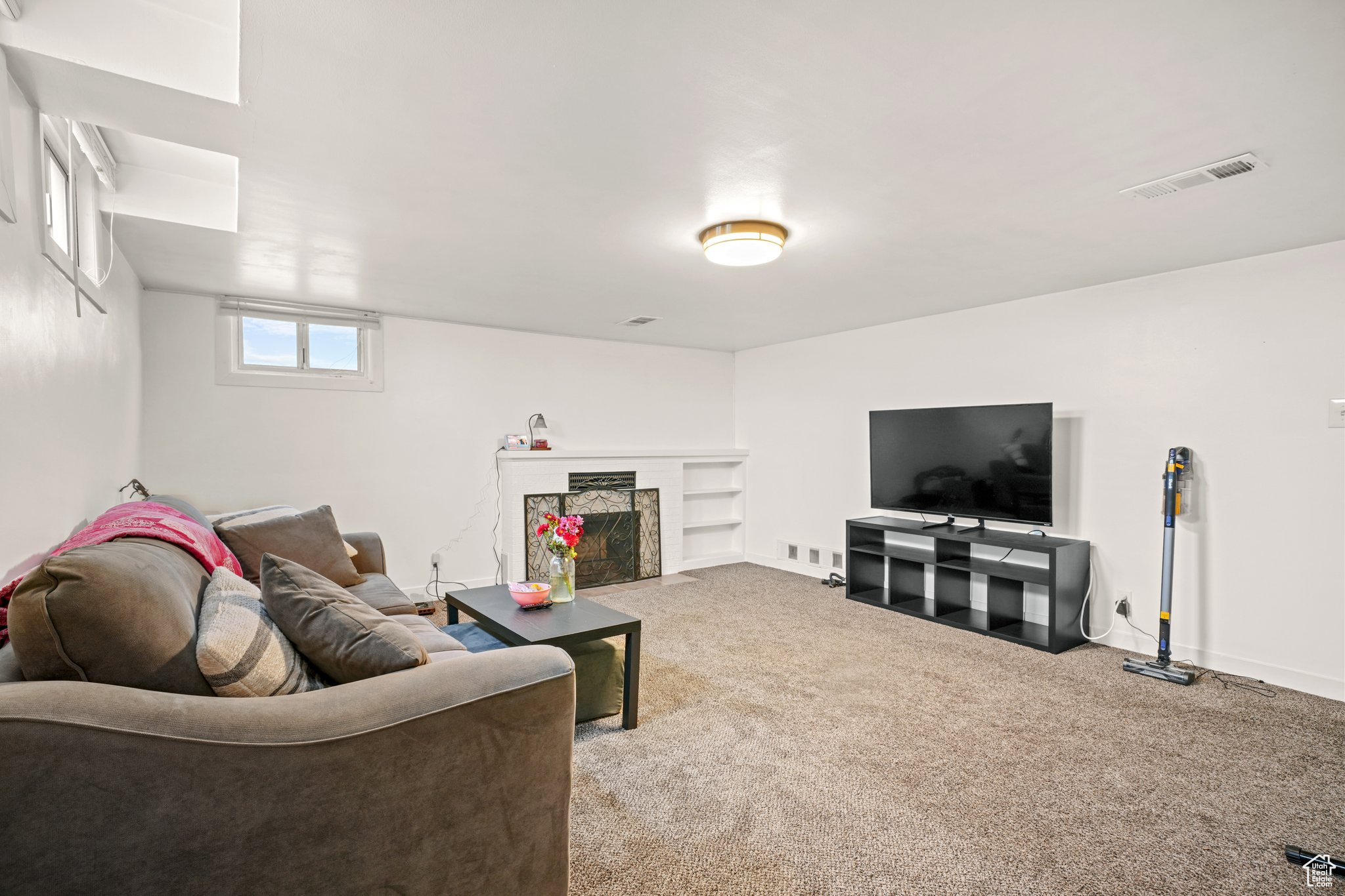 Carpeted living area featuring a fireplace with flush hearth, visible vents, and baseboards