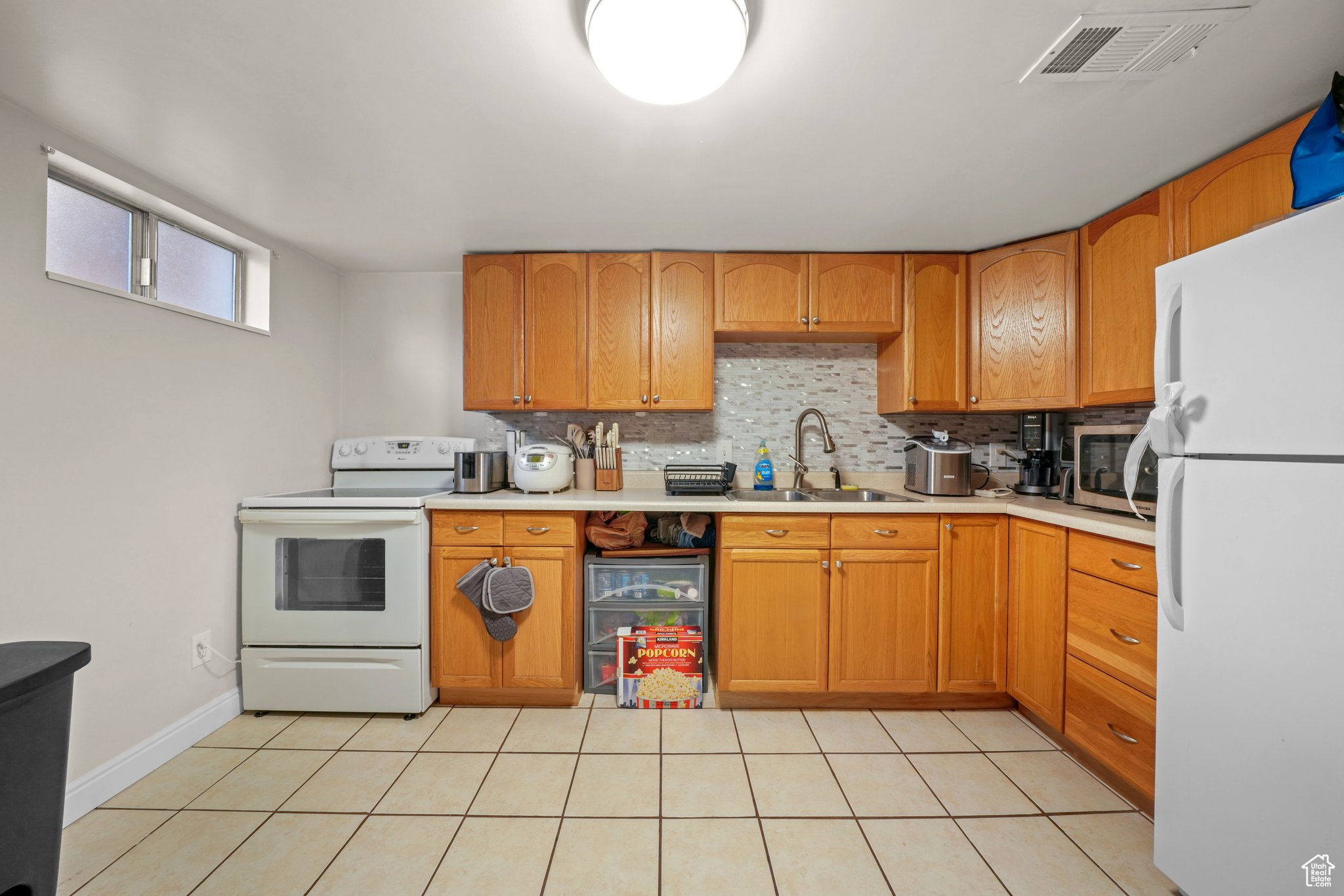 Kitchen with light countertops, visible vents, backsplash, a sink, and white appliances