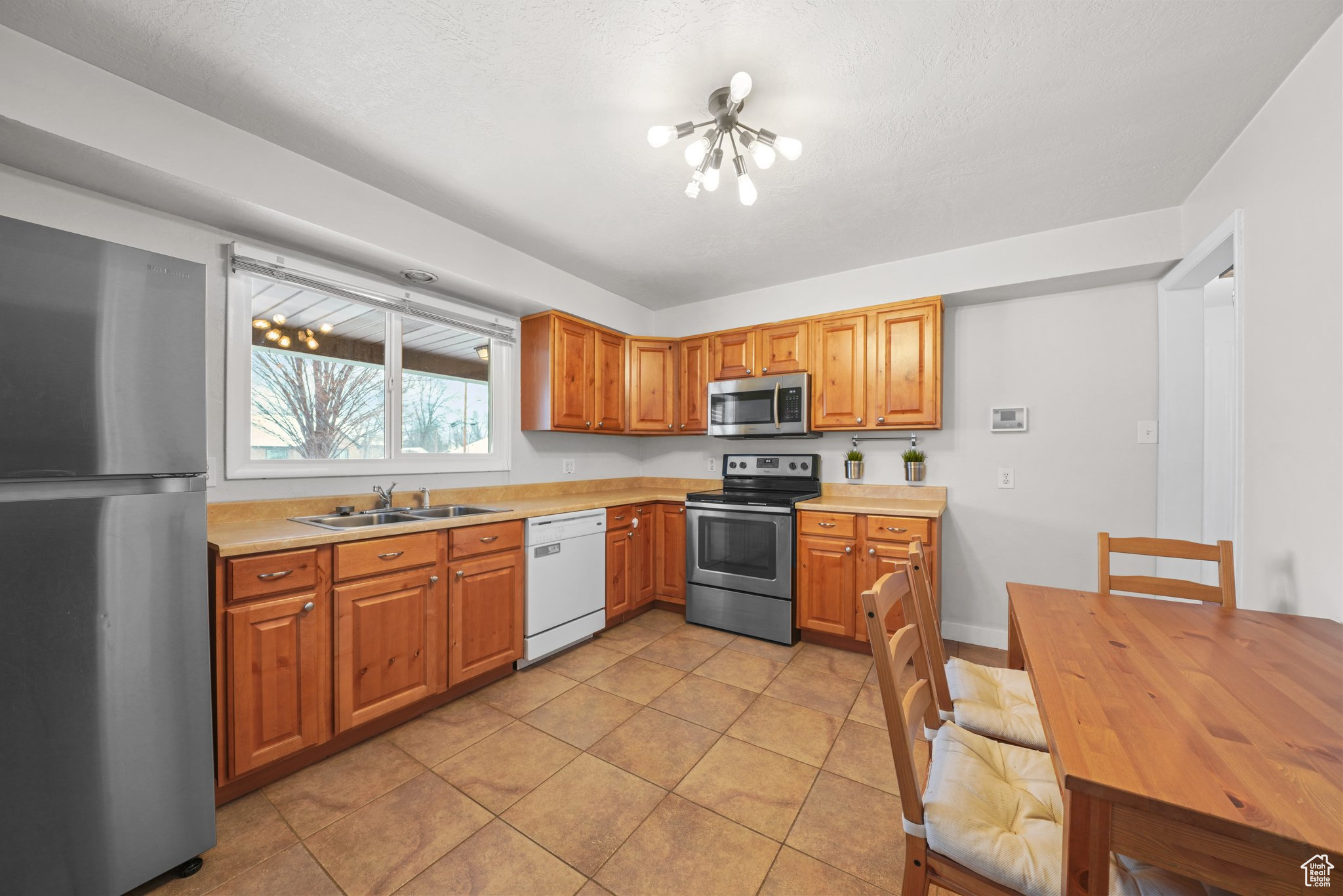 Kitchen with light tile patterned floors, brown cabinets, stainless steel appliances, light countertops, and a sink