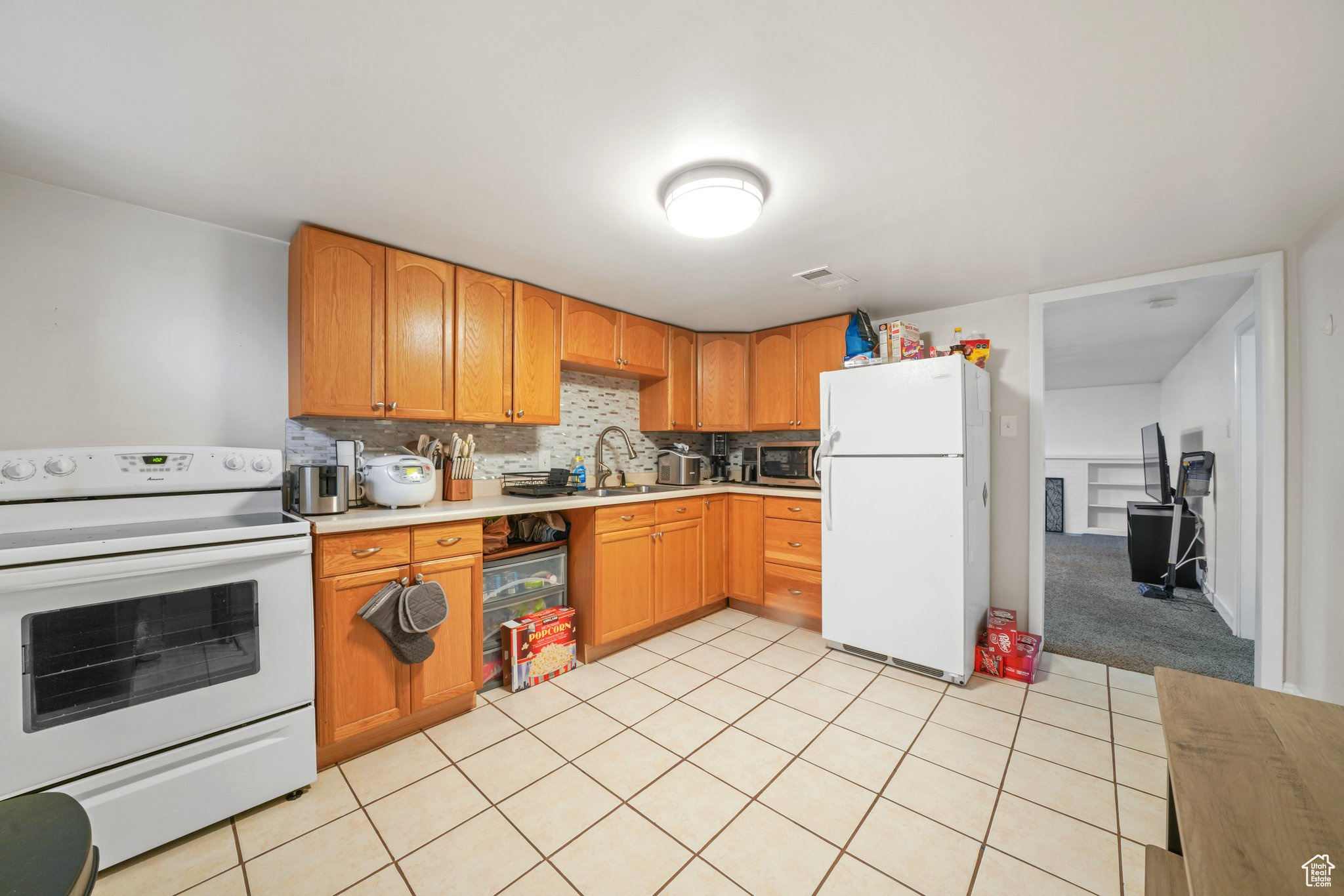 Kitchen with white appliances, tasteful backsplash, light tile patterned floors, light countertops, and a sink