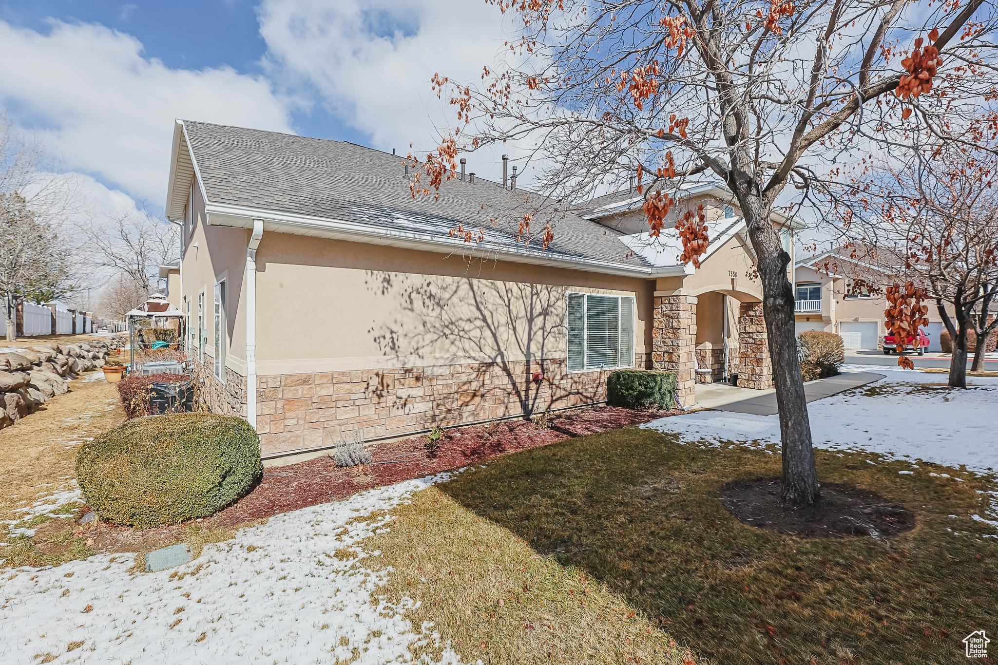 Snow covered property with a shingled roof, stone siding, a yard, and stucco siding
