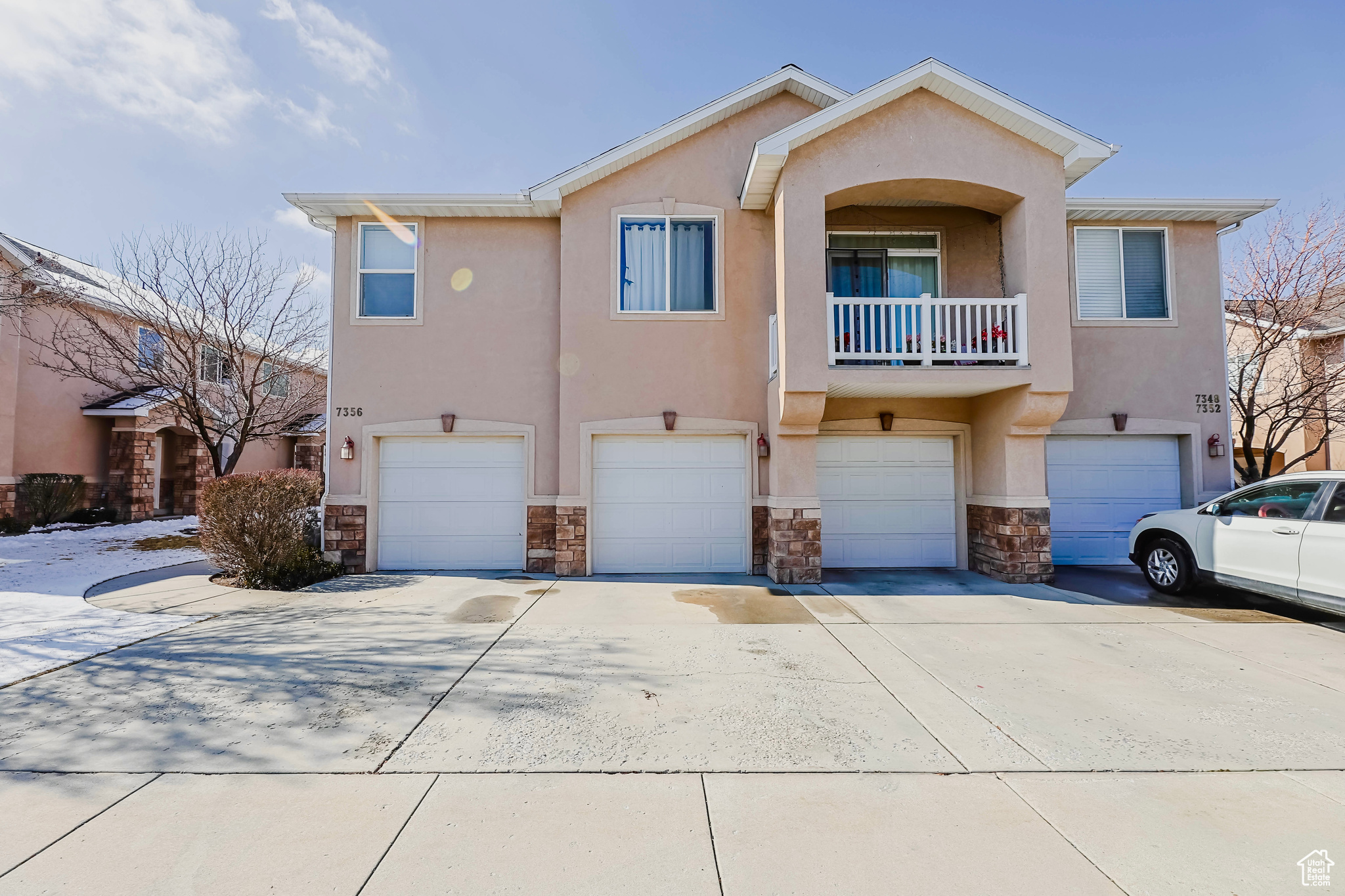 View of front of property featuring a garage, stone siding, driveway, and stucco siding
