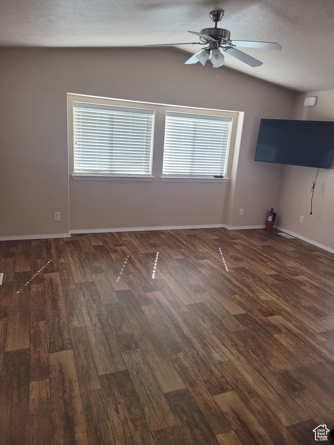 Unfurnished room featuring lofted ceiling, ceiling fan, dark wood-style flooring, and baseboards