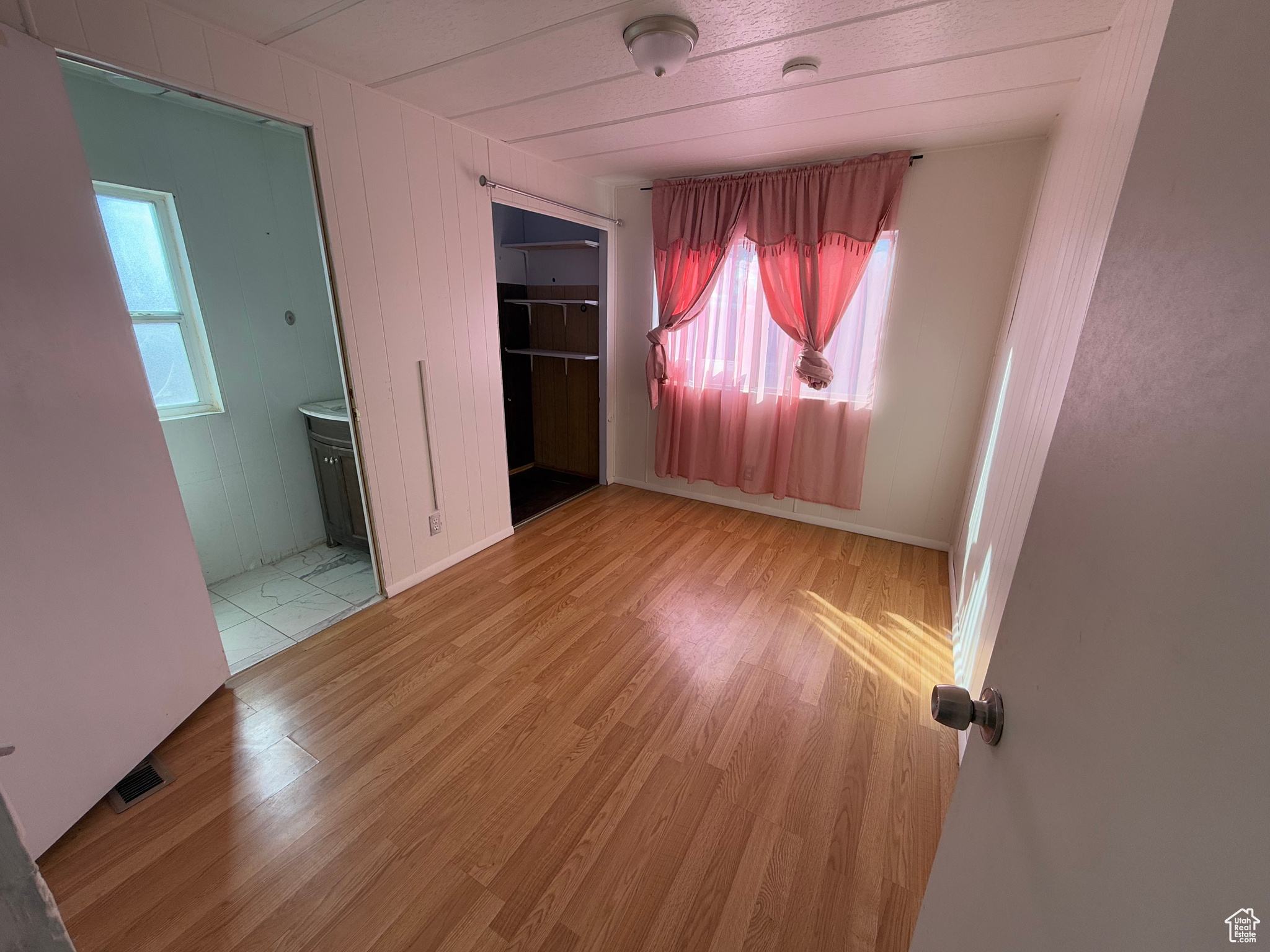 Unfurnished bedroom with light wood finished floors, a closet, ensuite bath, and a walk in closet