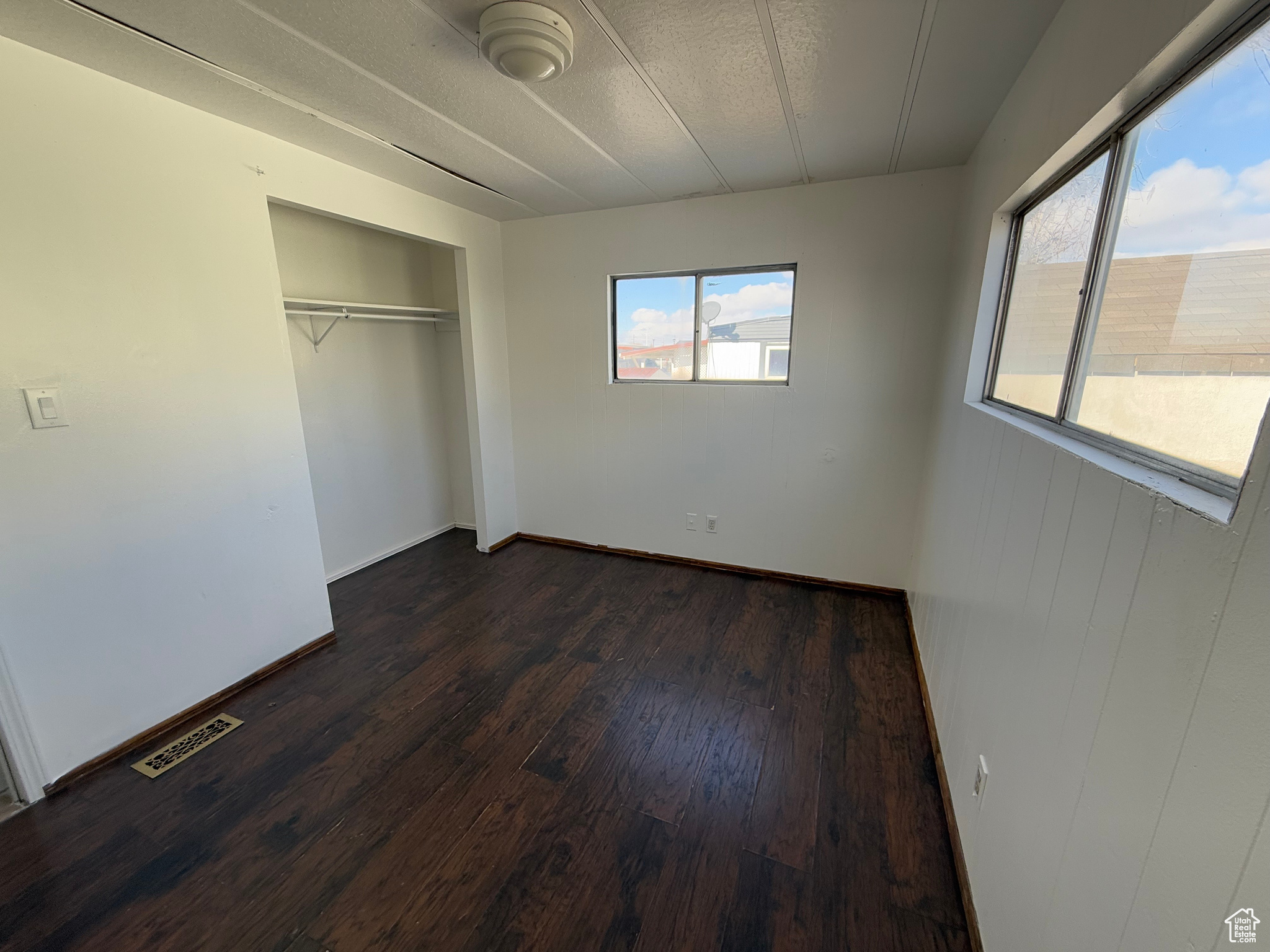 Unfurnished bedroom featuring a closet, visible vents, dark wood finished floors, and baseboards