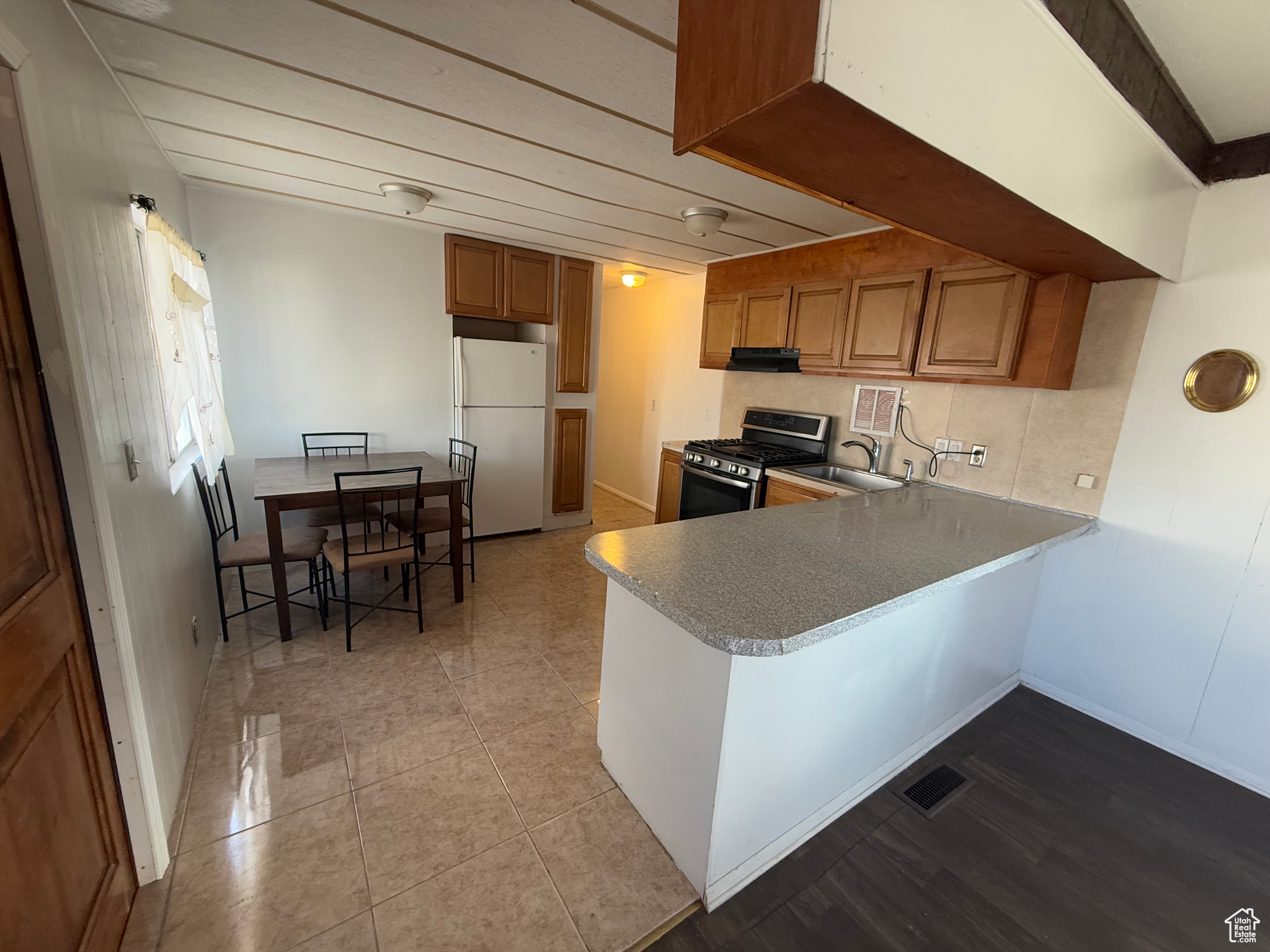 Kitchen featuring light countertops, brown cabinetry, freestanding refrigerator, stainless steel range with gas stovetop, and a peninsula