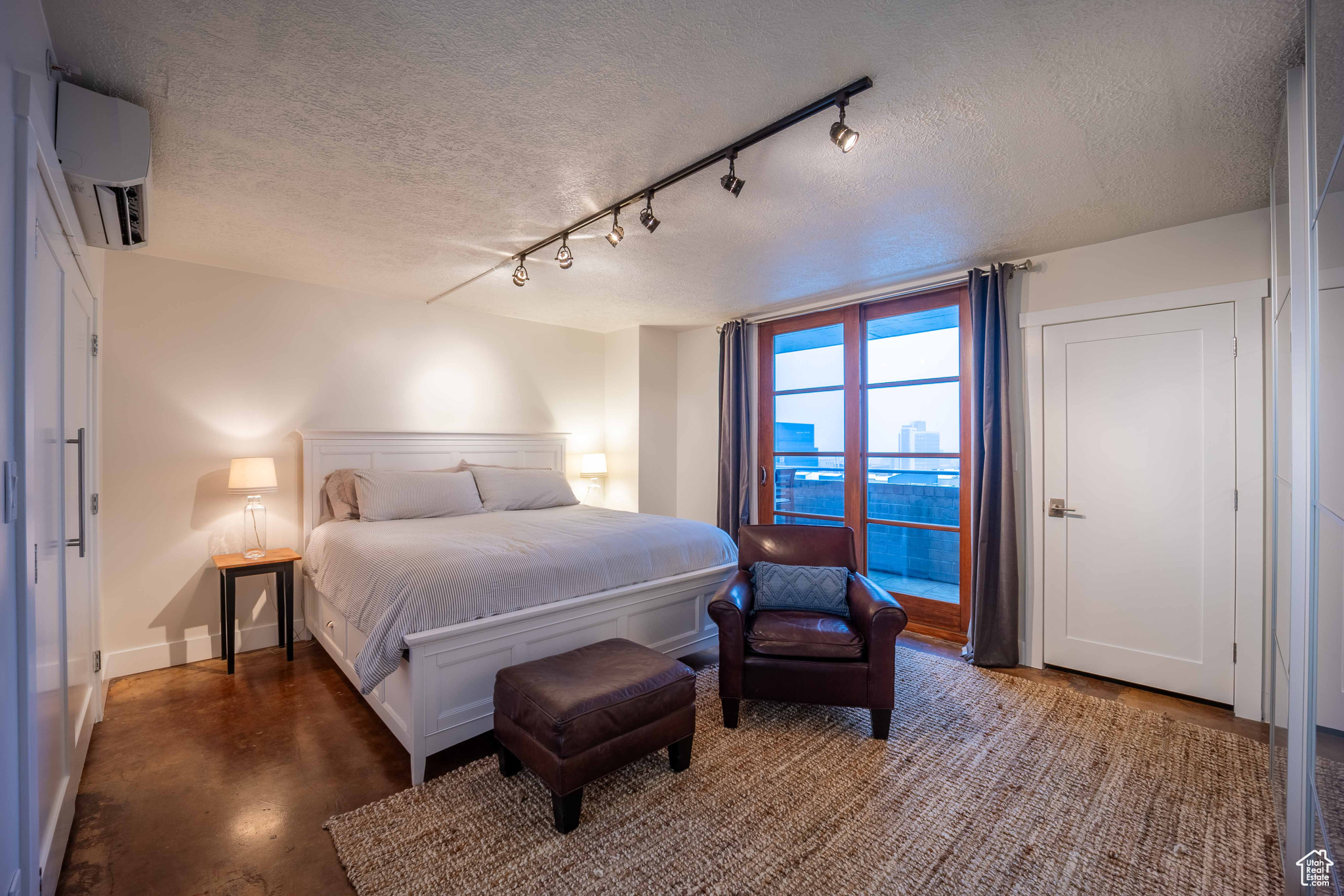 Bedroom featuring a textured ceiling, a wall unit AC, baseboards, and concrete flooring