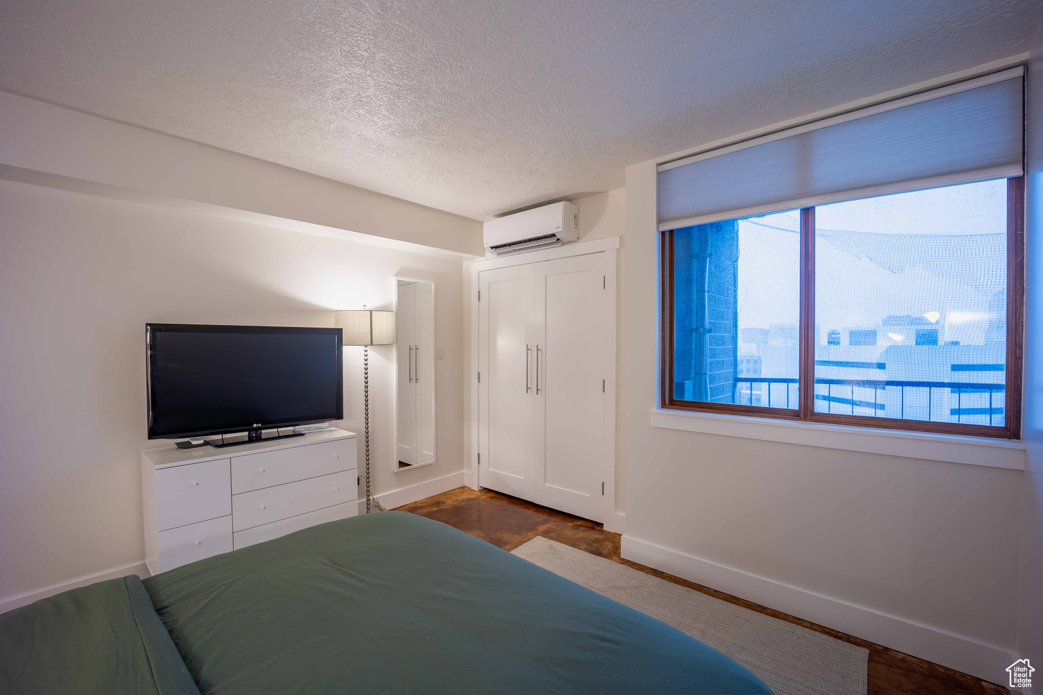 Unfurnished bedroom with a textured ceiling, an AC wall unit, and baseboards