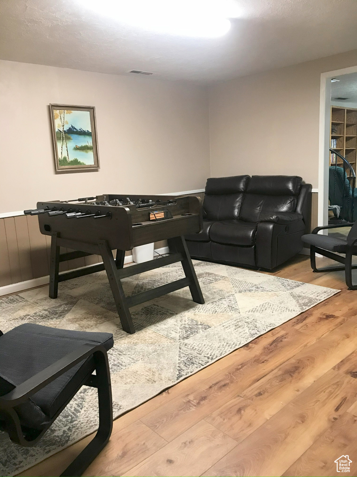 Rec room with light wood-type flooring, a wainscoted wall, and visible vents