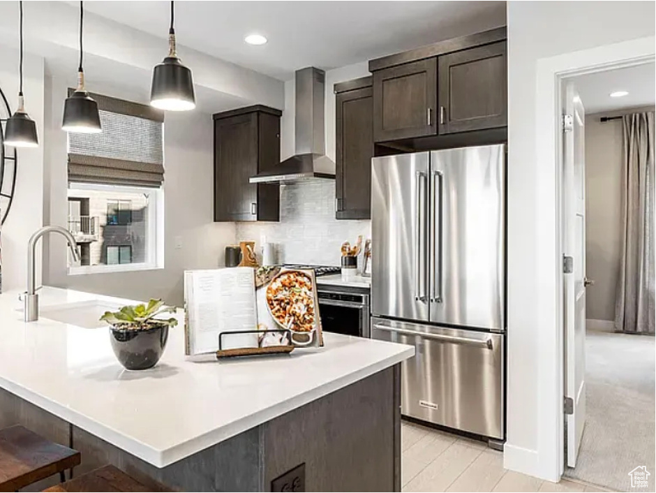 Kitchen featuring stainless steel appliances, light countertops, and wall chimney range hood