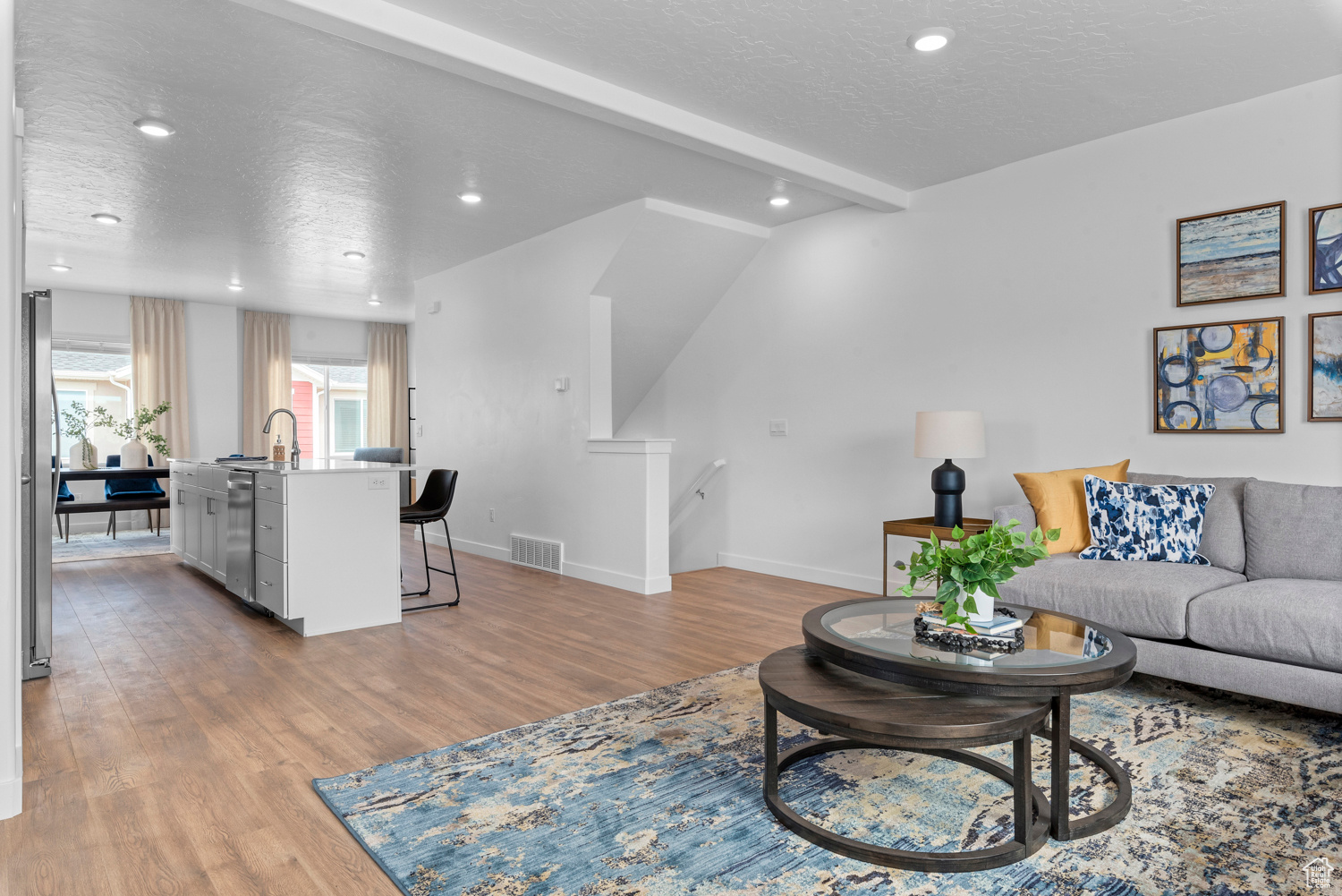 Living area featuring a textured ceiling, visible vents, baseboards, light wood-type flooring, and beam ceiling