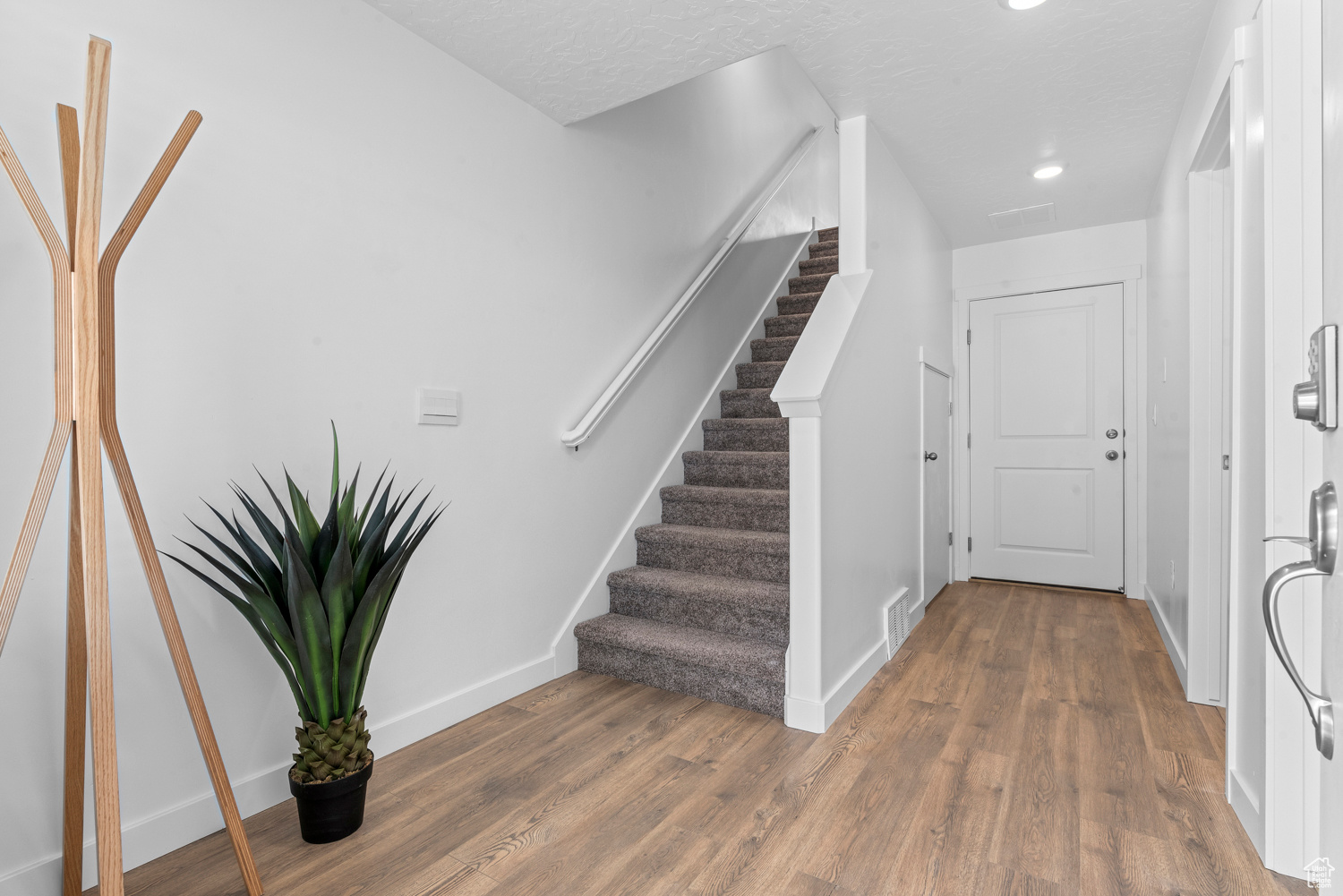 Foyer featuring dark wood-style floors, visible vents, a textured ceiling, baseboards, and stairs