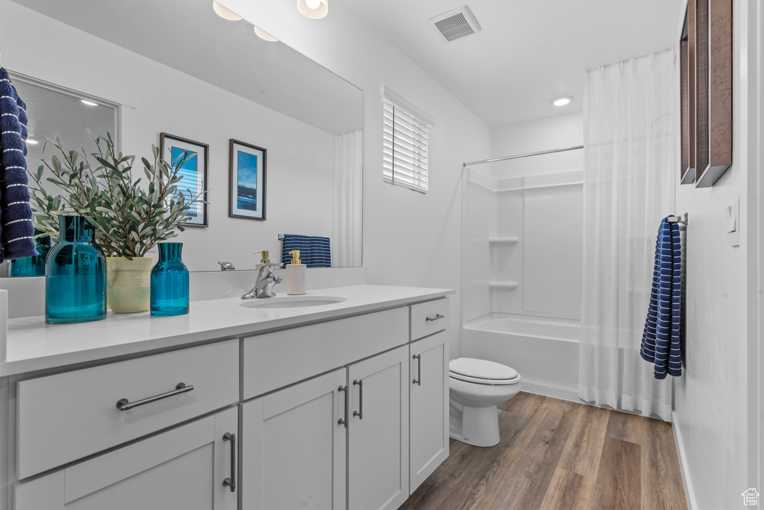 Full bath featuring visible vents, shower / bathtub combination with curtain, toilet, vanity, and wood finished floors
