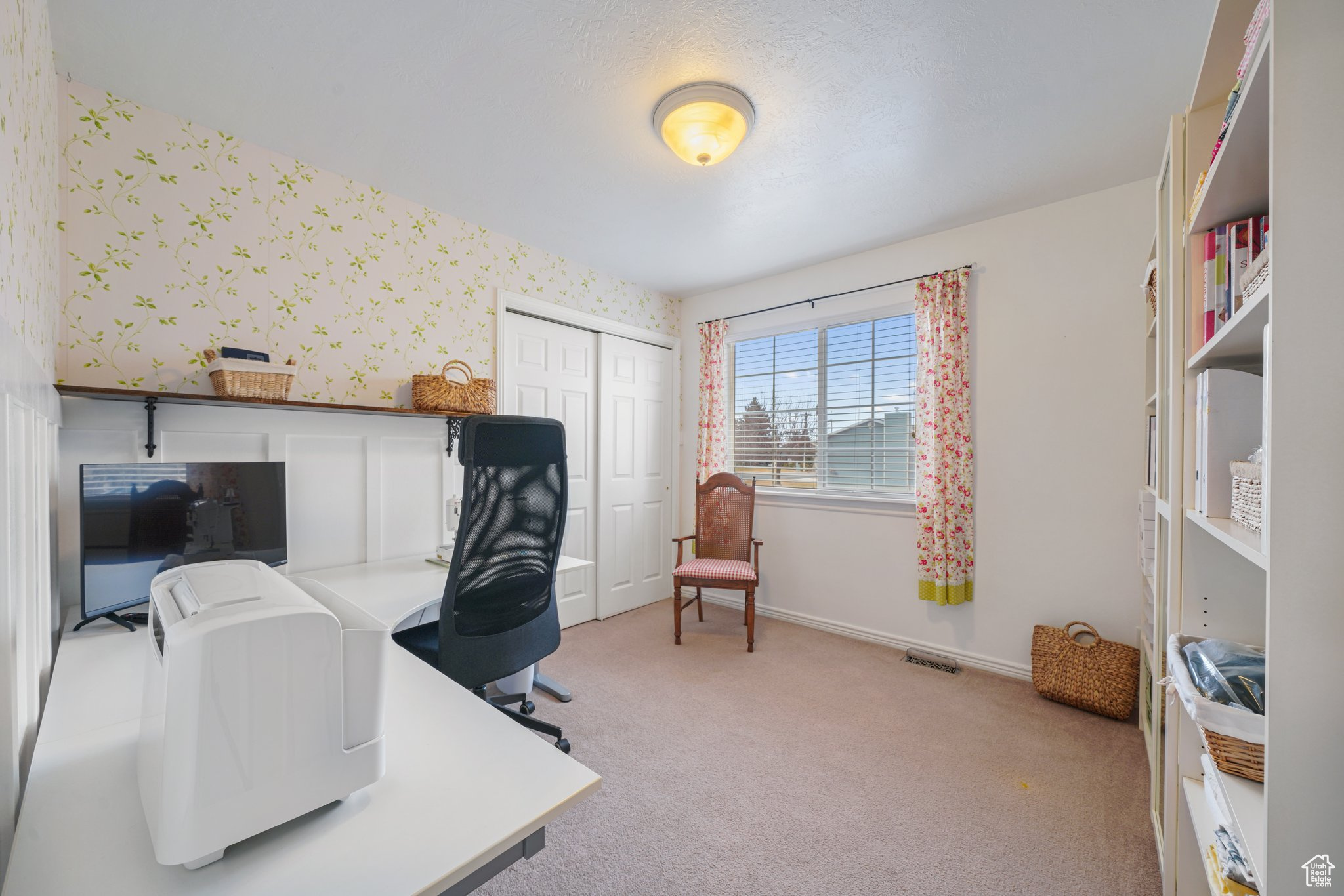 Office area with light carpet, wallpapered walls, visible vents, and baseboards