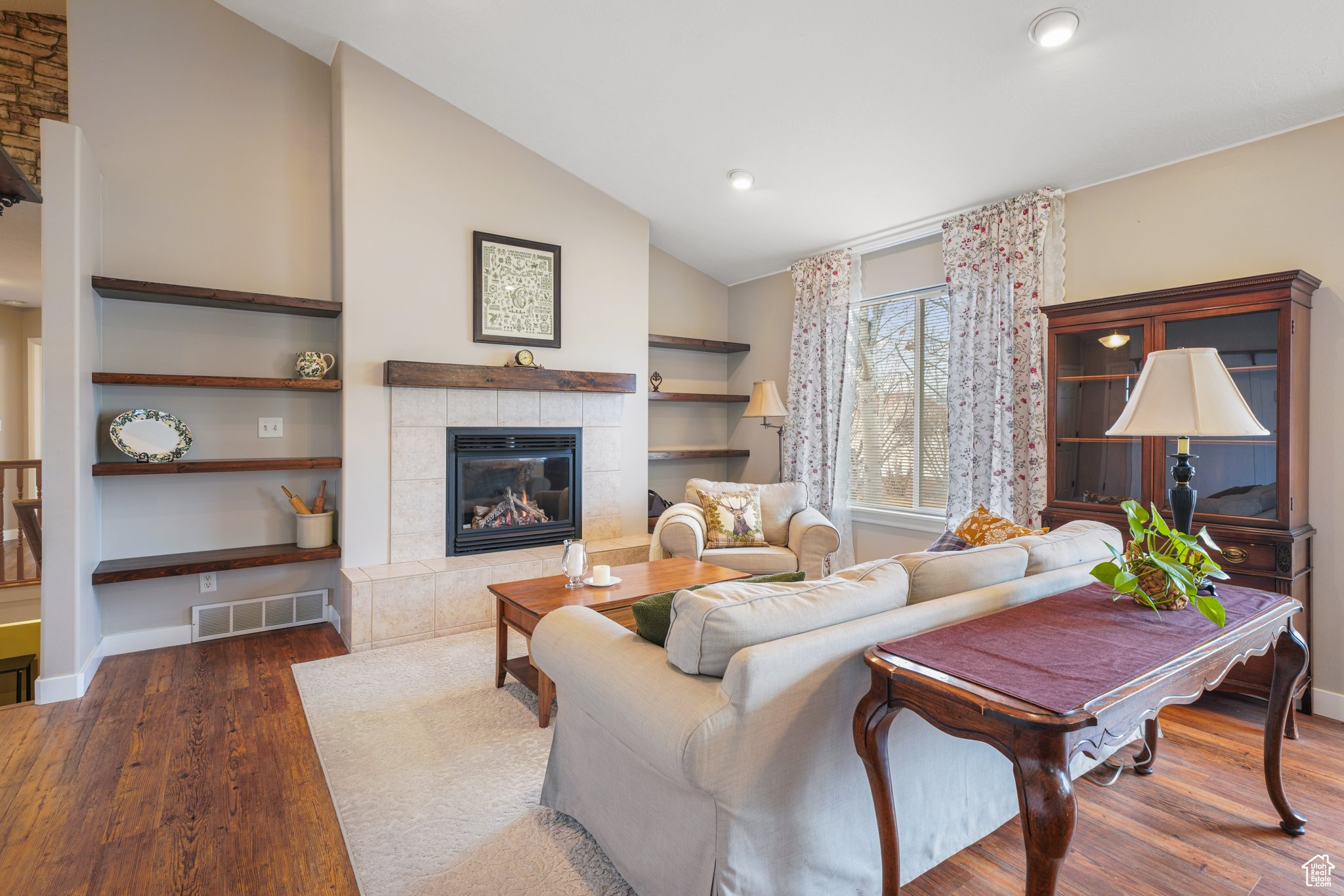 Living area with baseboards, visible vents, a tile fireplace, dark wood-type flooring, and vaulted ceiling