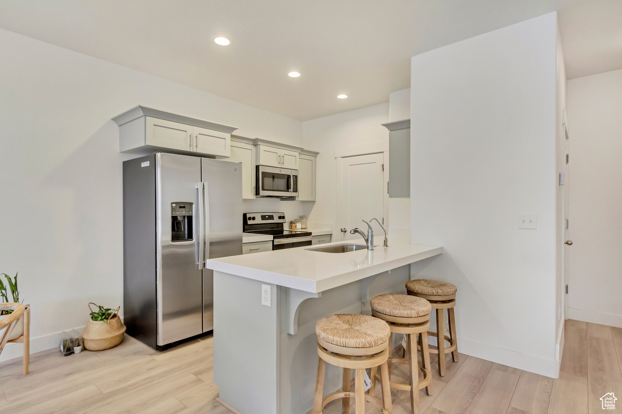 Kitchen featuring a breakfast bar area, appliances with stainless steel finishes, light countertops, gray cabinetry, and a sink