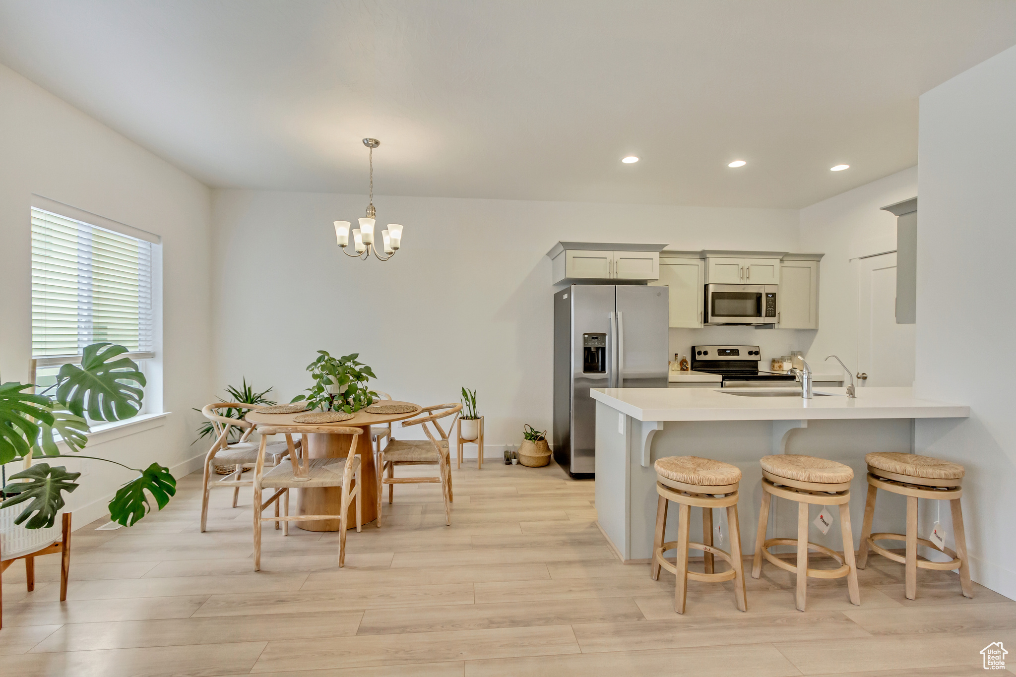 Kitchen with decorative light fixtures, stainless steel appliances, light countertops, a chandelier, and light wood-type flooring