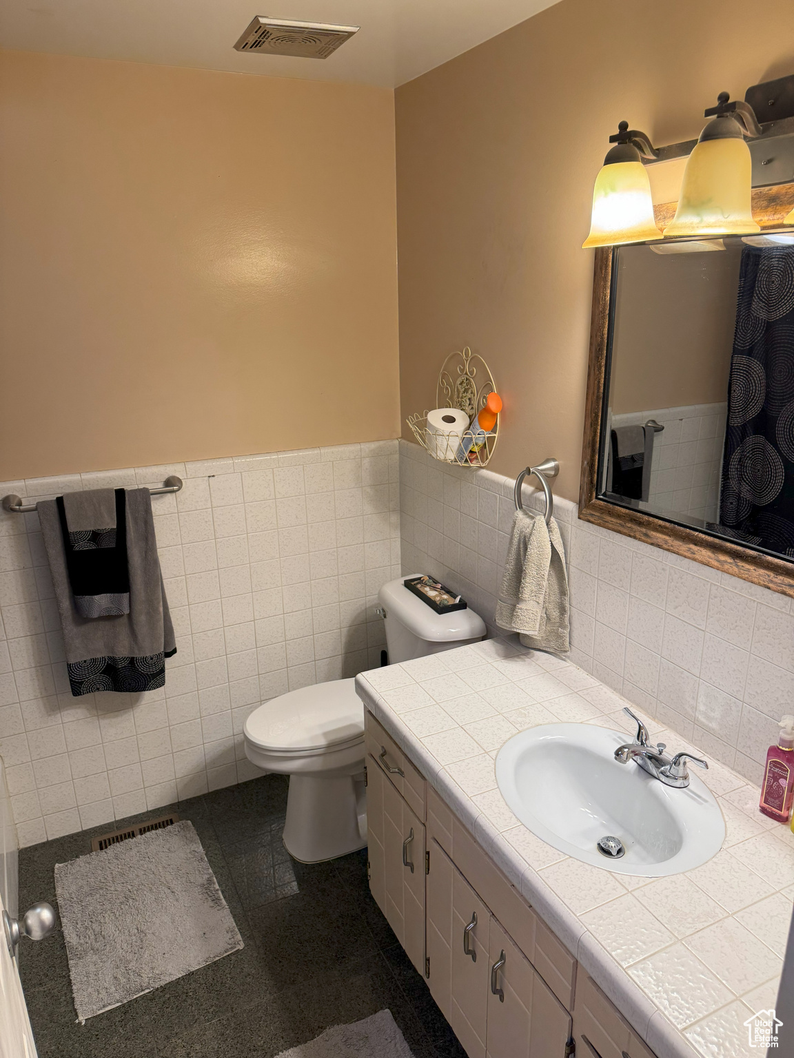 Bathroom featuring tile walls, visible vents, toilet, wainscoting, and vanity