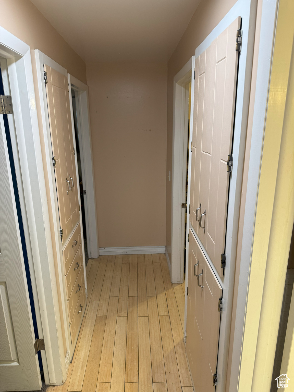 Hallway featuring two built-in linen cabinets, light wood-style floors and baseboards