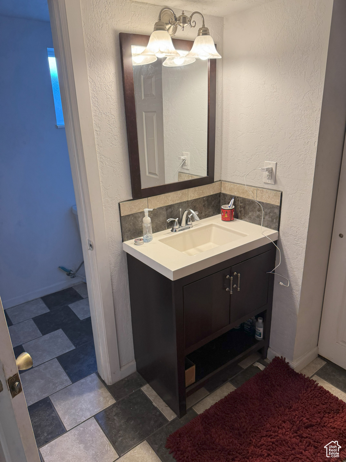 Bathroom featuring a textured wall, backsplash, vanity, and baseboards