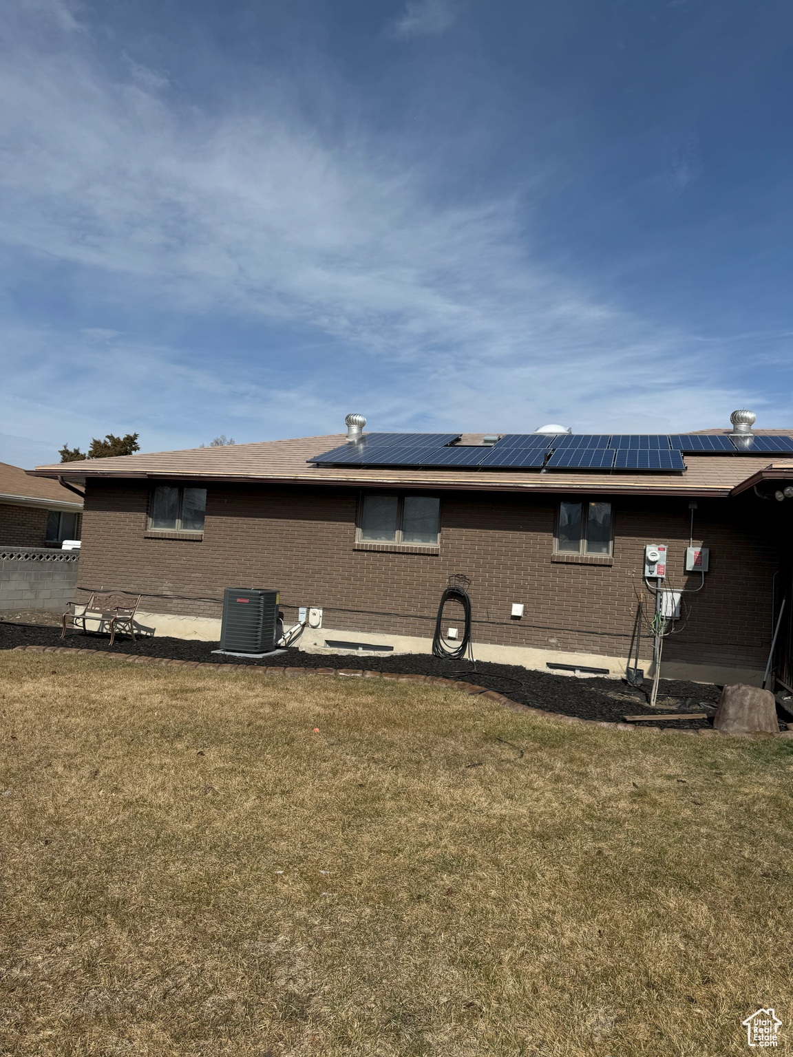 Rear view of property featuring solar panels, brick siding, a lawn, and central air condition unit