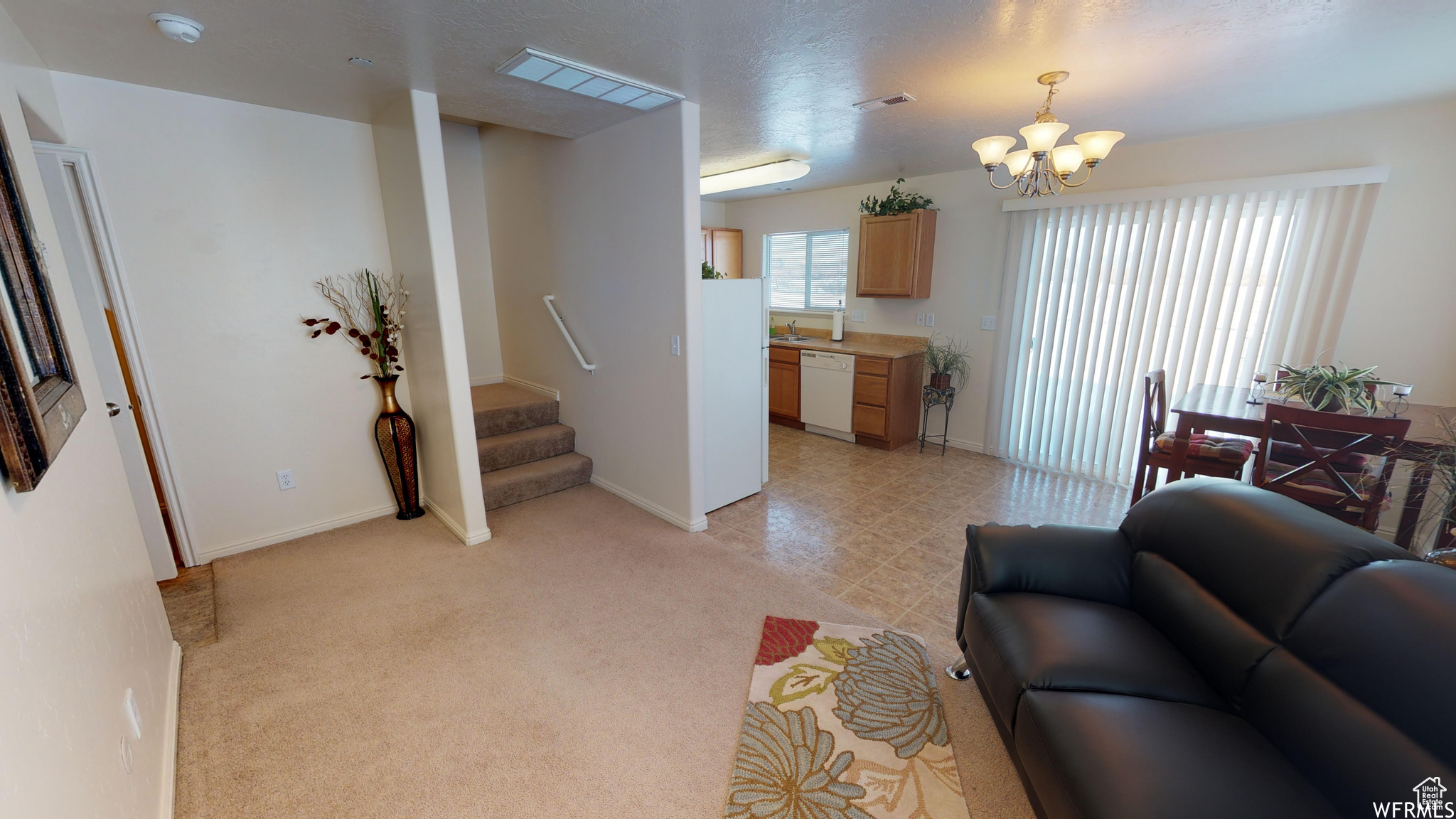 Living room featuring baseboards, visible vents, light colored carpet, an inviting chandelier, and stairs