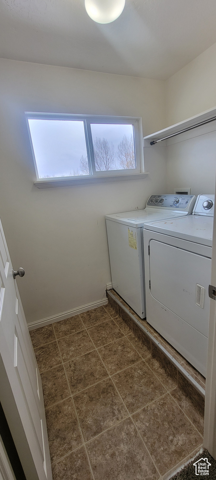 Clothes washing area with laundry area, washing machine and dryer, baseboards, and dark tile patterned flooring