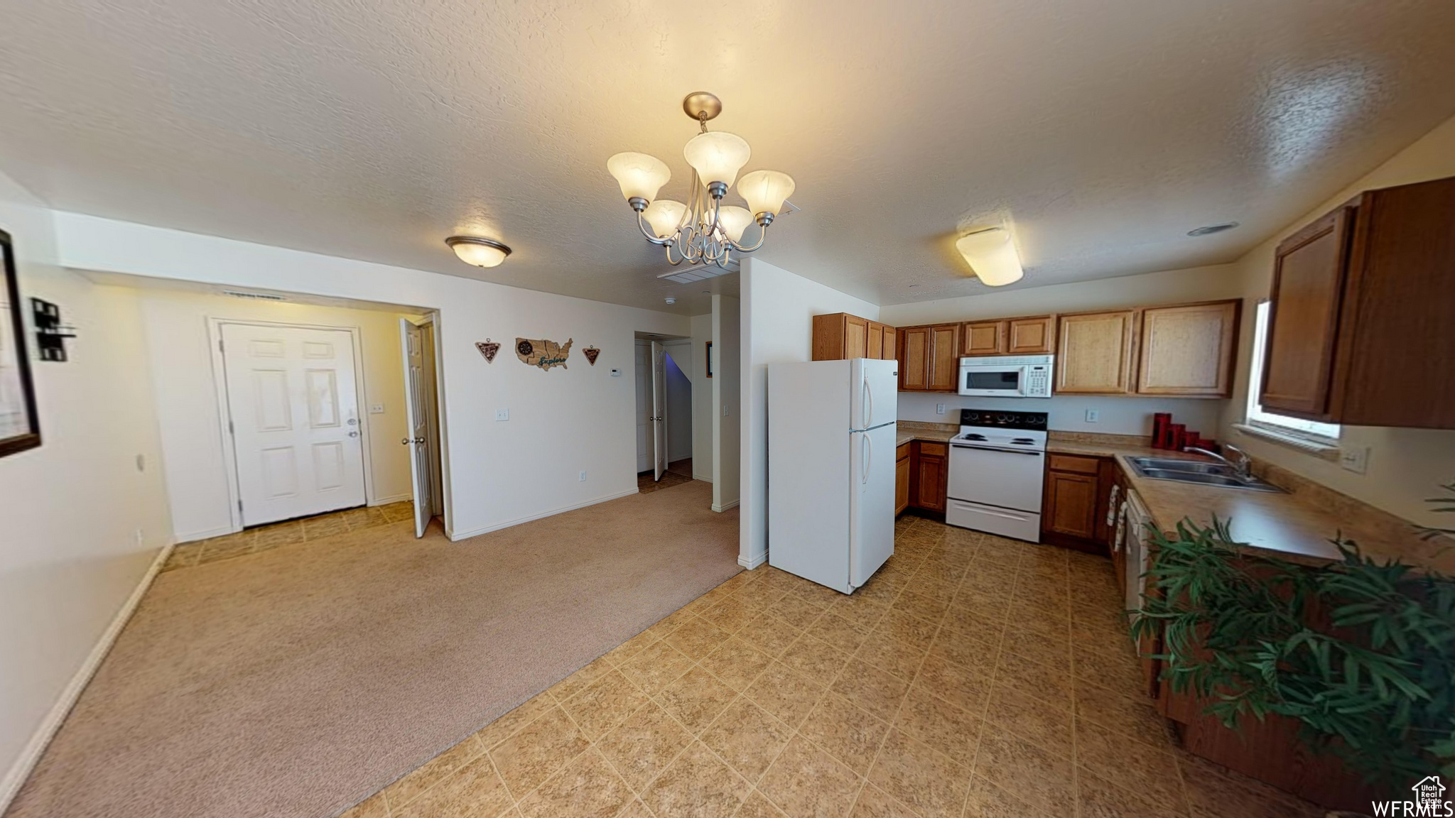 Kitchen featuring light colored carpet, white appliances, a sink, light countertops, and brown cabinetry