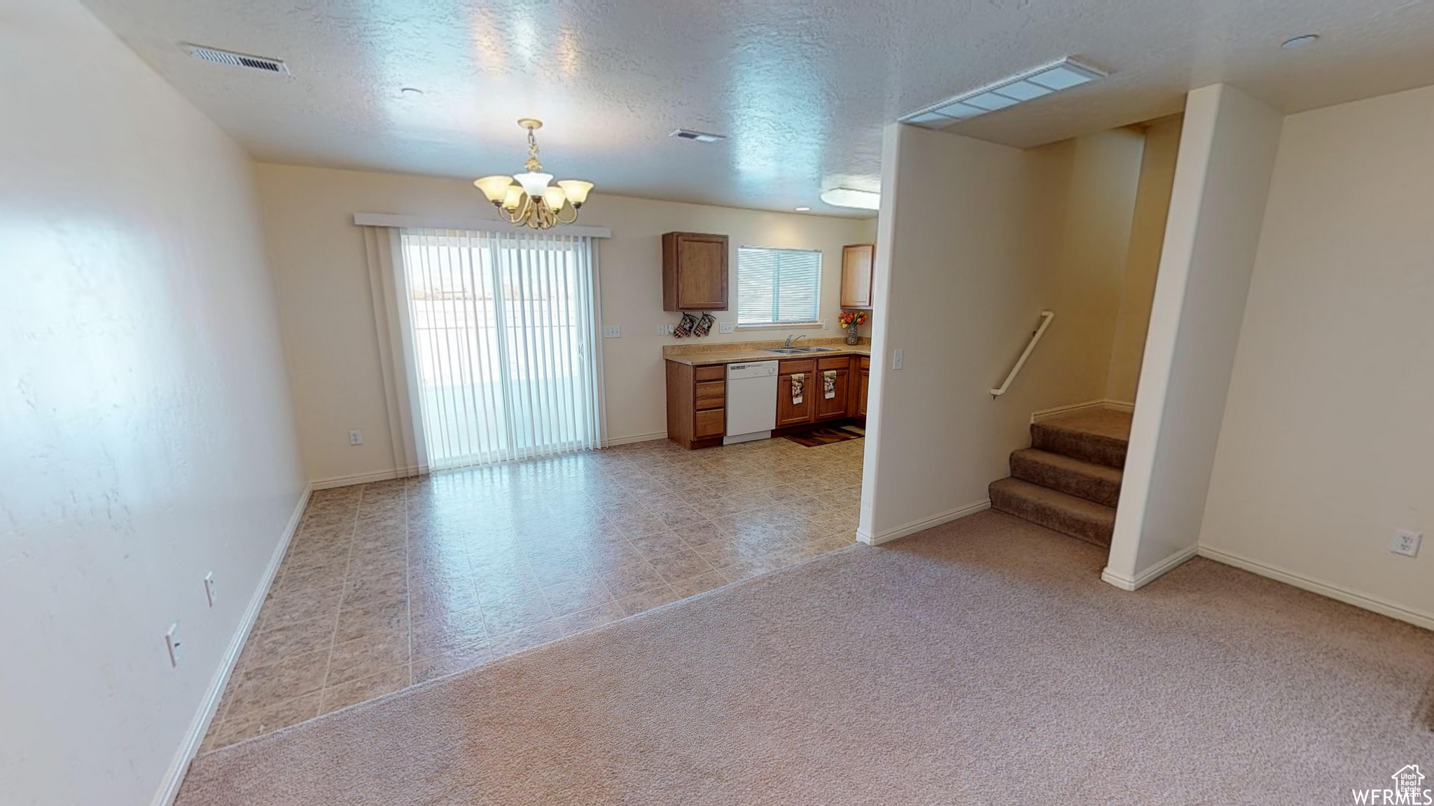 Unfurnished living room with a textured ceiling, a chandelier, light carpet, visible vents, and stairs