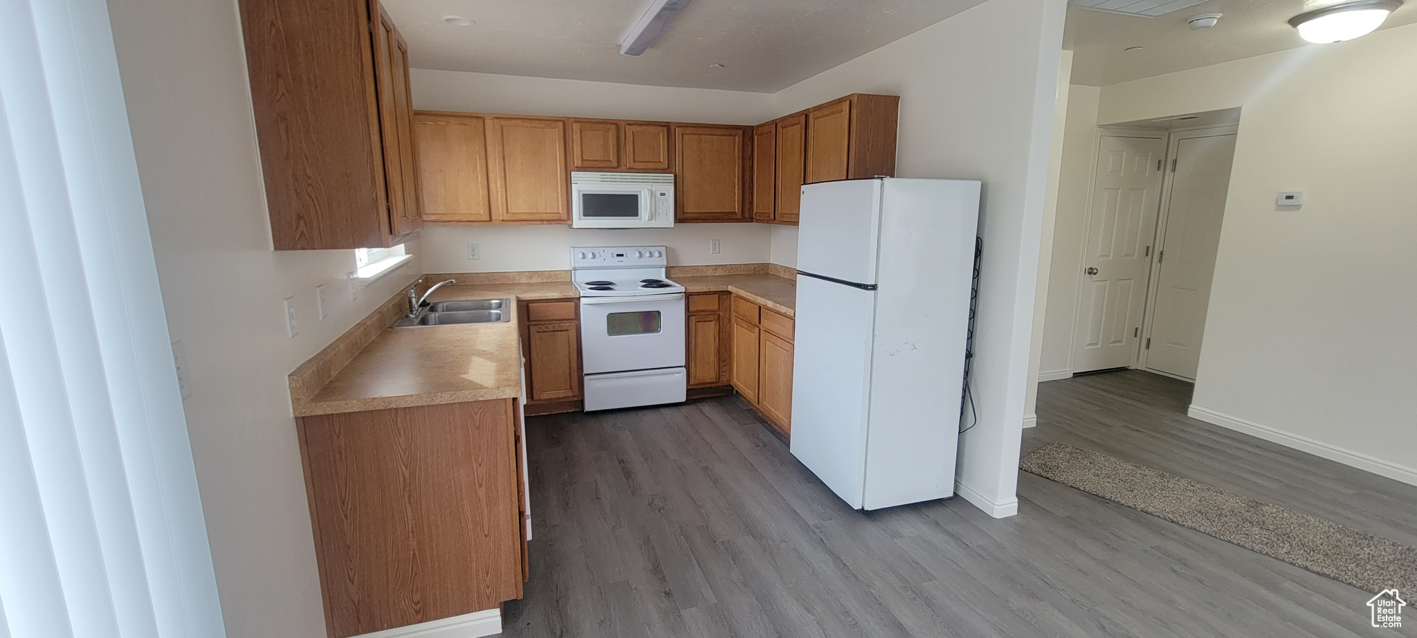 Kitchen with brown cabinets, white appliances, light countertops, and a sink