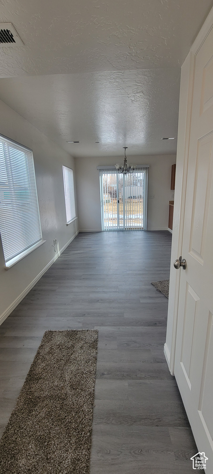 Unfurnished room featuring a textured ceiling, a notable chandelier, visible vents, baseboards, and dark wood finished floors