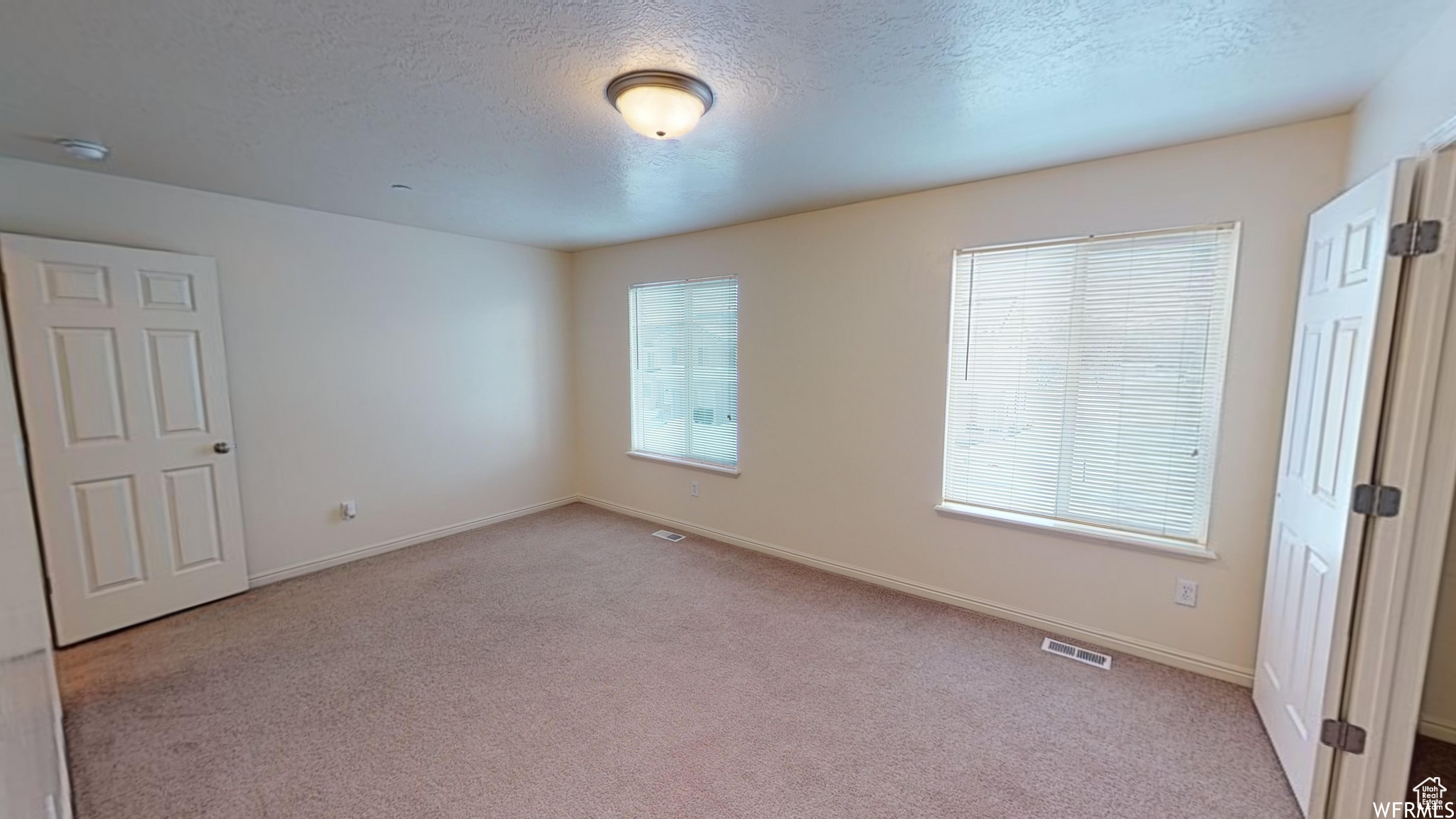 Unfurnished room featuring baseboards, visible vents, a textured ceiling, and light colored carpet