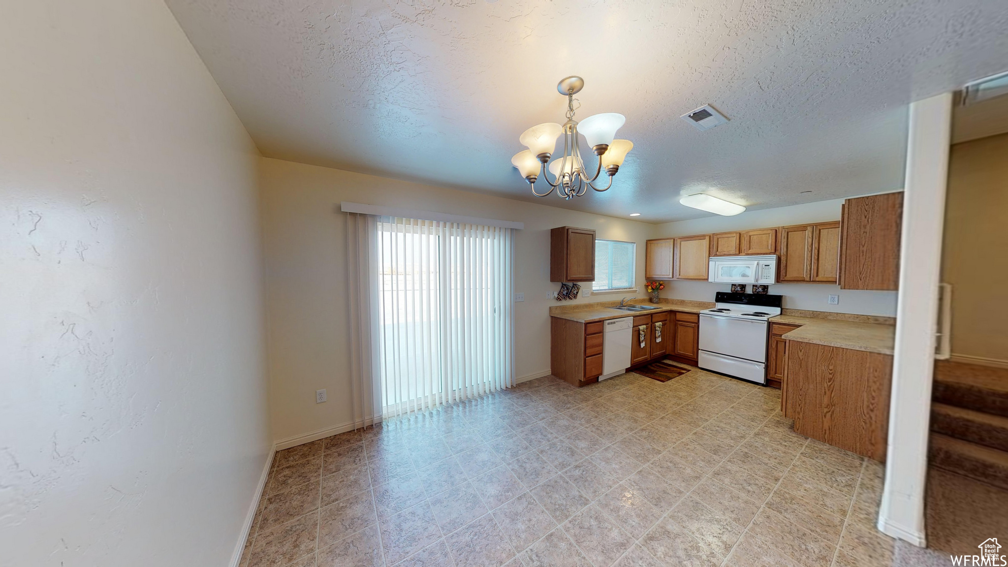 Kitchen featuring light countertops, hanging light fixtures, visible vents, a chandelier, and white appliances