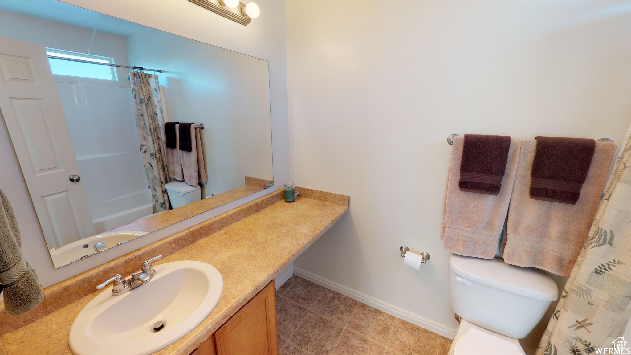 Full bathroom with shower / tub combo with curtain, toilet, vanity, tile patterned flooring, and baseboards