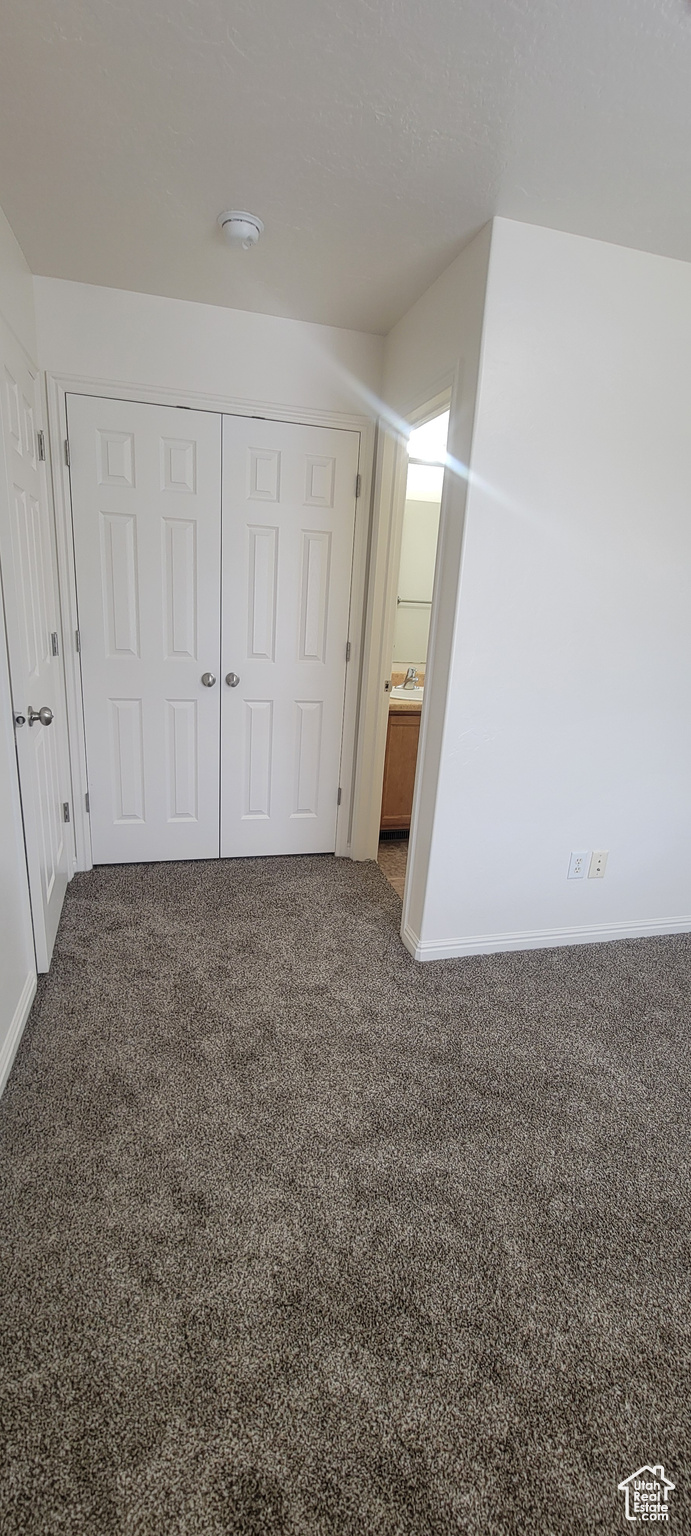 Unfurnished bedroom with dark colored carpet, a closet, and baseboards