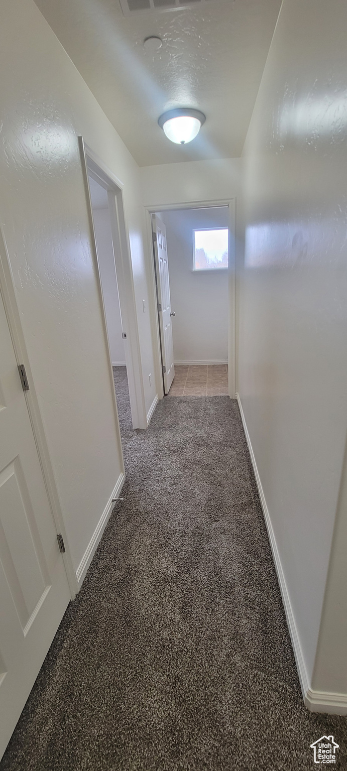 Hallway featuring a textured ceiling, baseboards, and light colored carpet