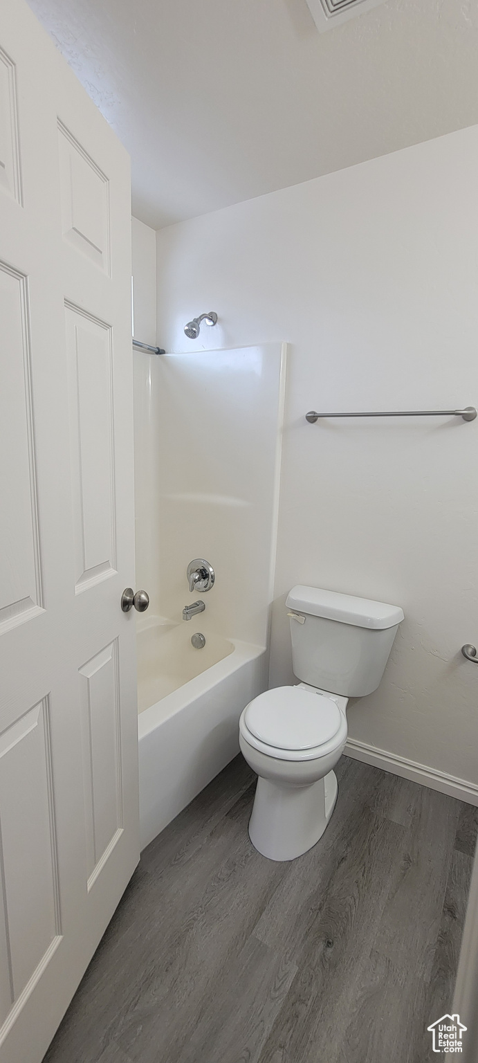 Bathroom featuring baseboards, toilet, shower / tub combination, and wood finished floors