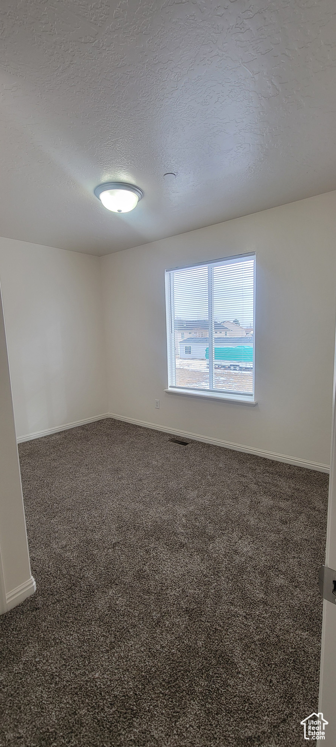 Spare room featuring a textured ceiling, dark colored carpet, visible vents, and baseboards