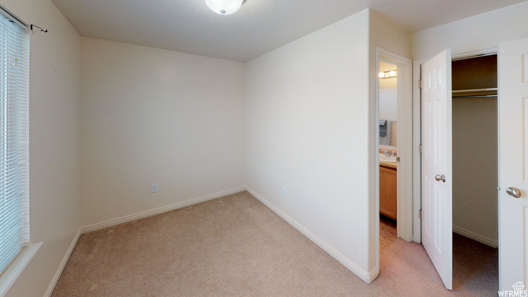 Unfurnished bedroom with a closet, light colored carpet, connected bathroom, and baseboards