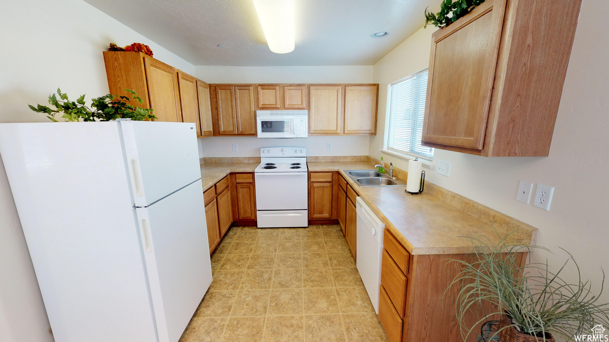 Kitchen featuring white appliances, light tile patterned floors, light countertops, and a sink