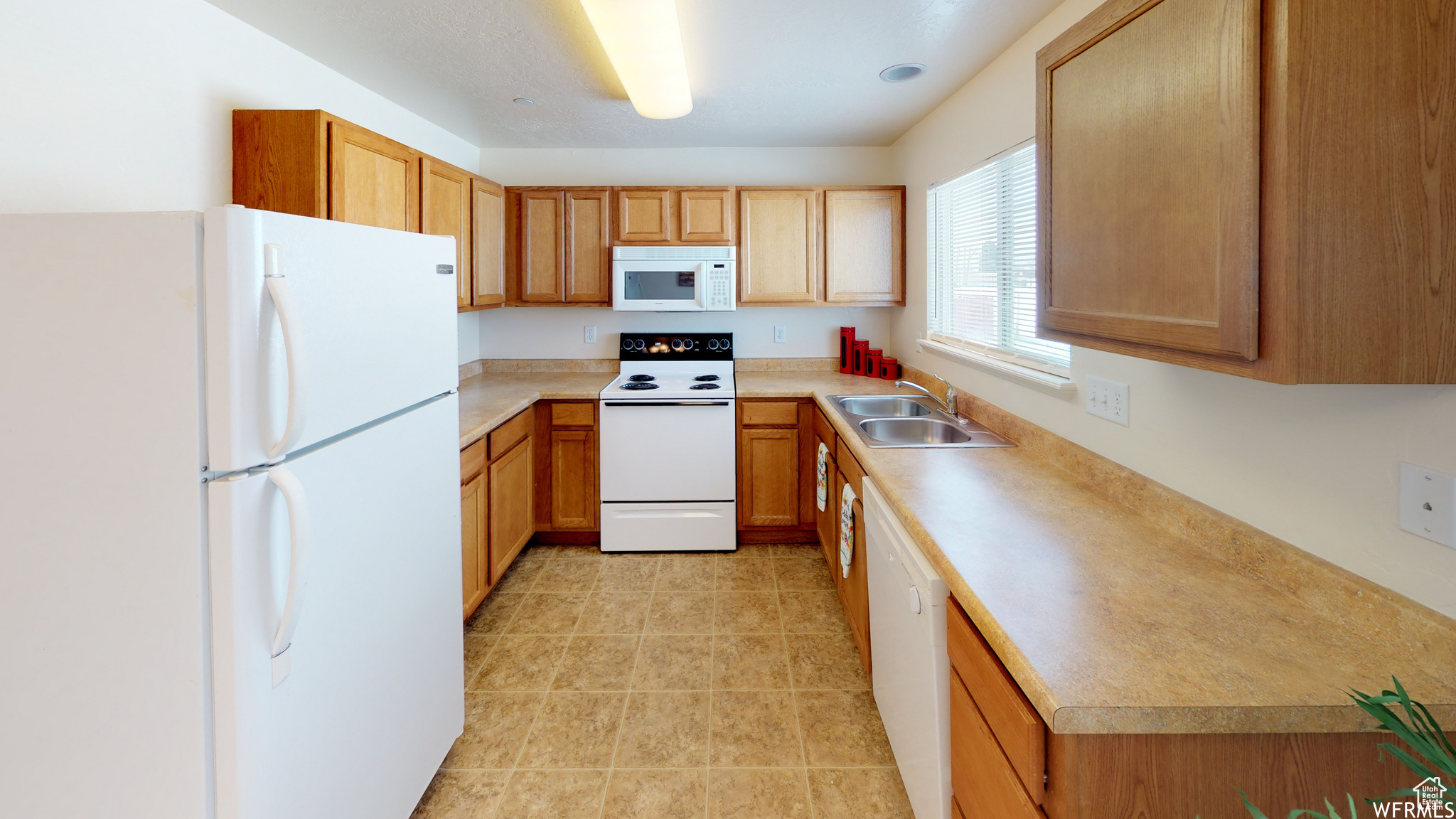 Kitchen featuring light countertops, white appliances, light tile patterned flooring, and a sink