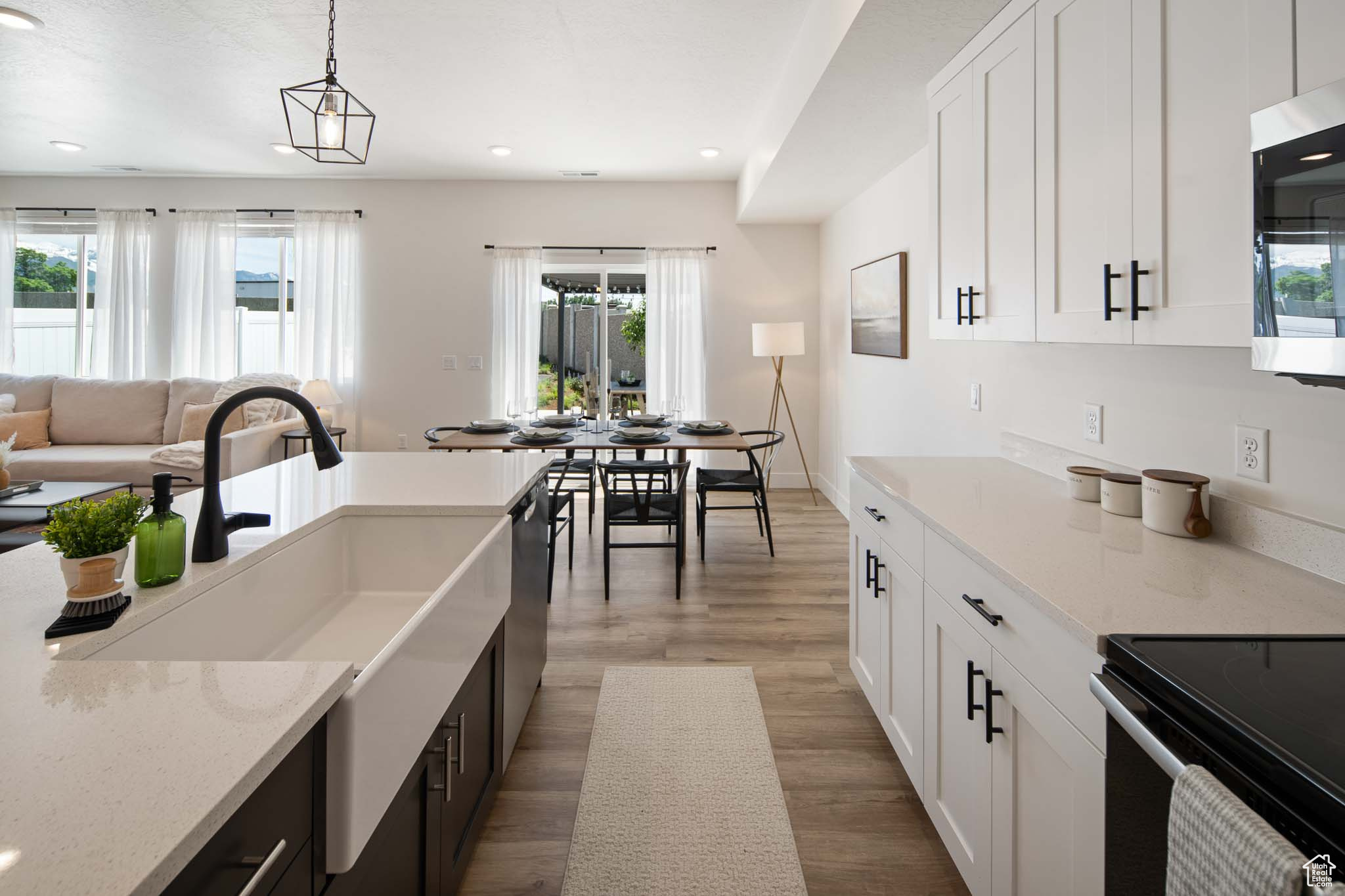 Kitchen featuring light stone counters, dark wood-type flooring, white cabinets, stainless steel microwave, and decorative light fixtures