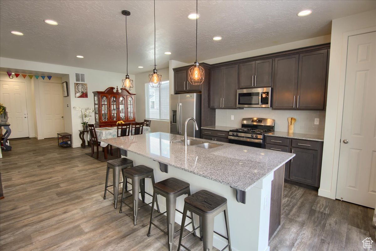 Kitchen with hanging light fixtures, appliances with stainless steel finishes, a breakfast bar, and a center island with sink