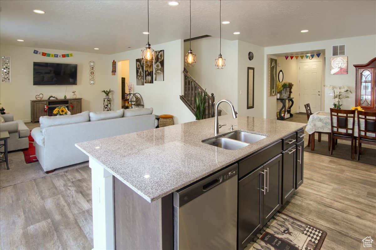 Kitchen featuring visible vents, an island with sink, decorative light fixtures, stainless steel dishwasher, and a sink