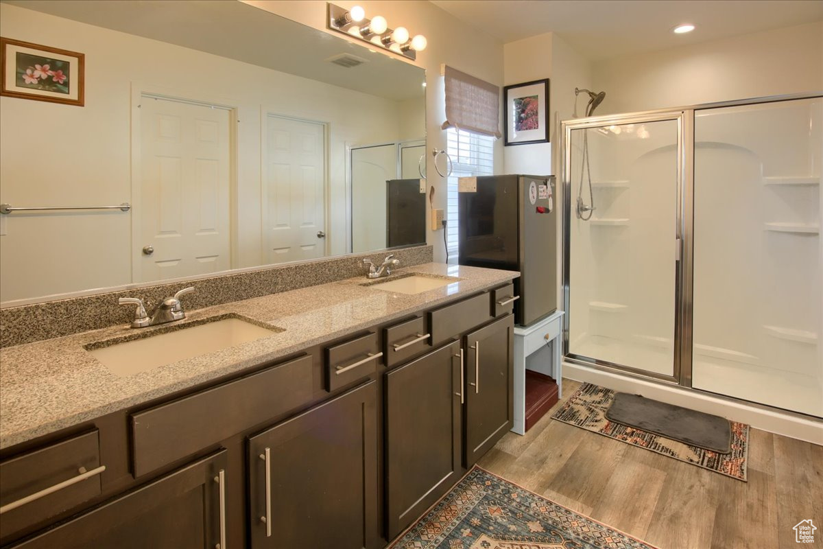 Full bathroom featuring double vanity, a shower stall, a sink, and wood finished floors