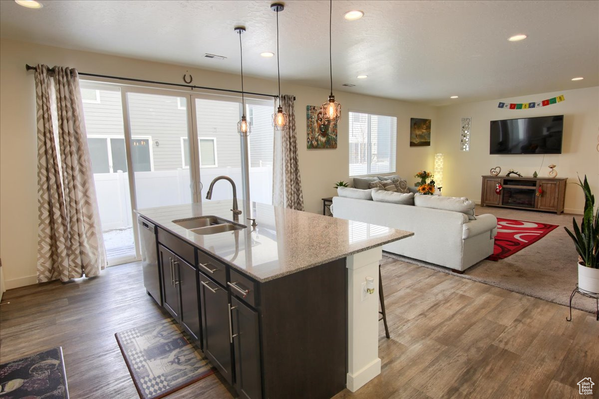 Kitchen with light stone counters, pendant lighting, stainless steel dishwasher, open floor plan, and a sink