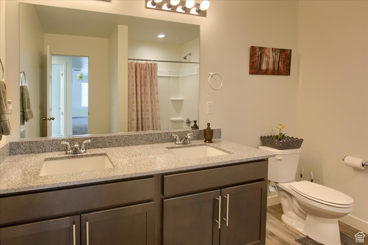 Bathroom with double vanity, a sink, toilet, and wood finished floors