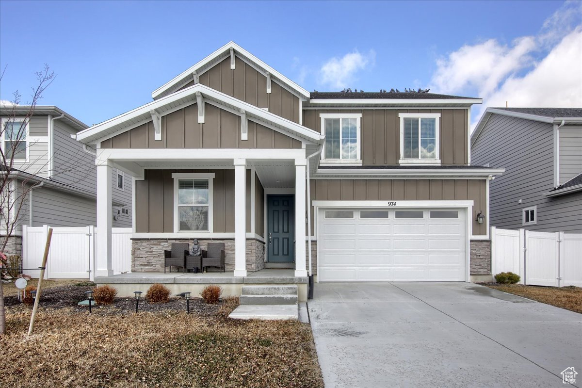 View of front facade featuring covered porch, stone siding, board and batten siding, and concrete driveway