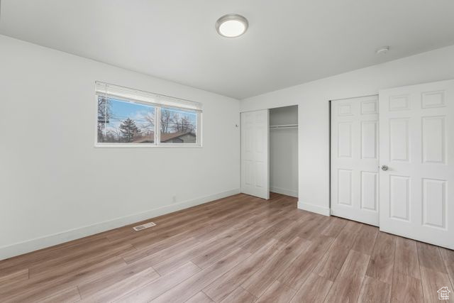 Unfurnished bedroom featuring light wood-style floors, visible vents, baseboards, and multiple closets